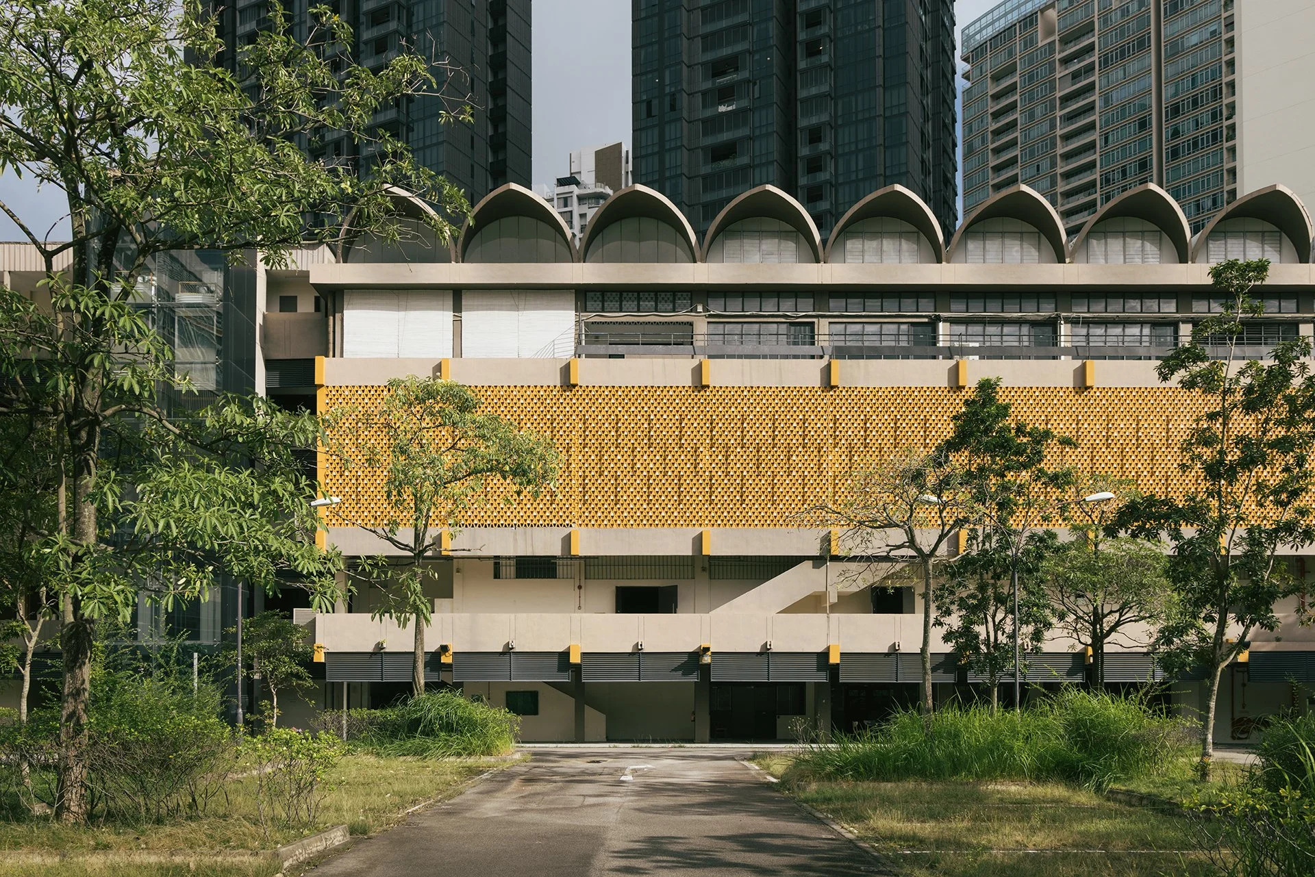 View of a modern building with unique architectural design featuring large arch-shaped roof structures, a yellow lattice facade, and surrounded by trees and greenery.
