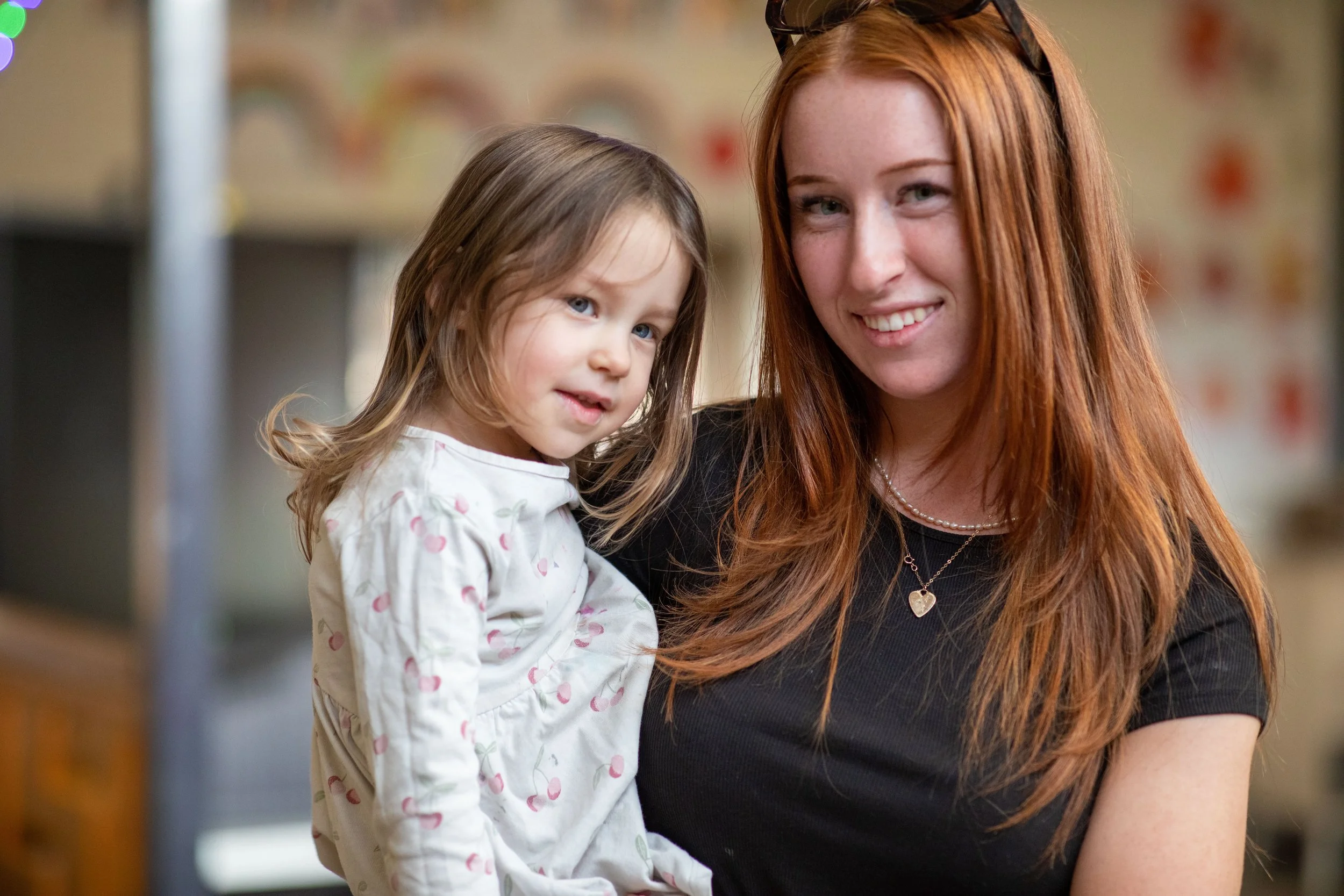 A woman with long red hair holding a young child with light brown hair in an indoor setting.