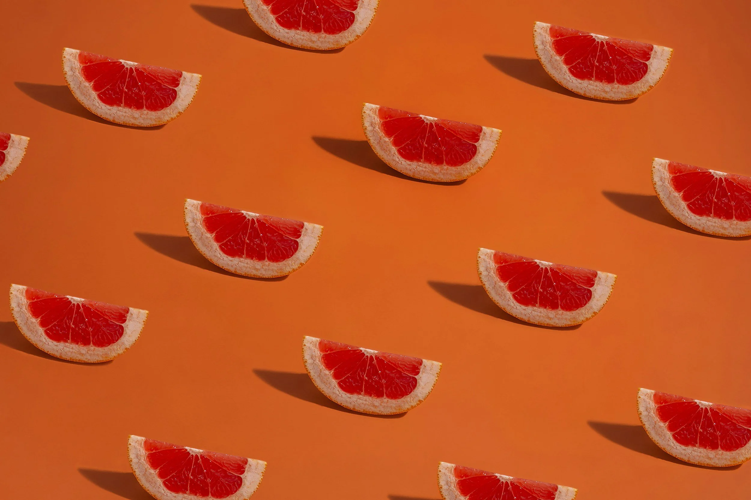 Slices of fresh red grapefruit arranged in a clean, repetitive geometric pattern on a vibrant orange background, beneath a modern lifestyle blog post title about pregnancy nutrition and evidence-based diet guides.