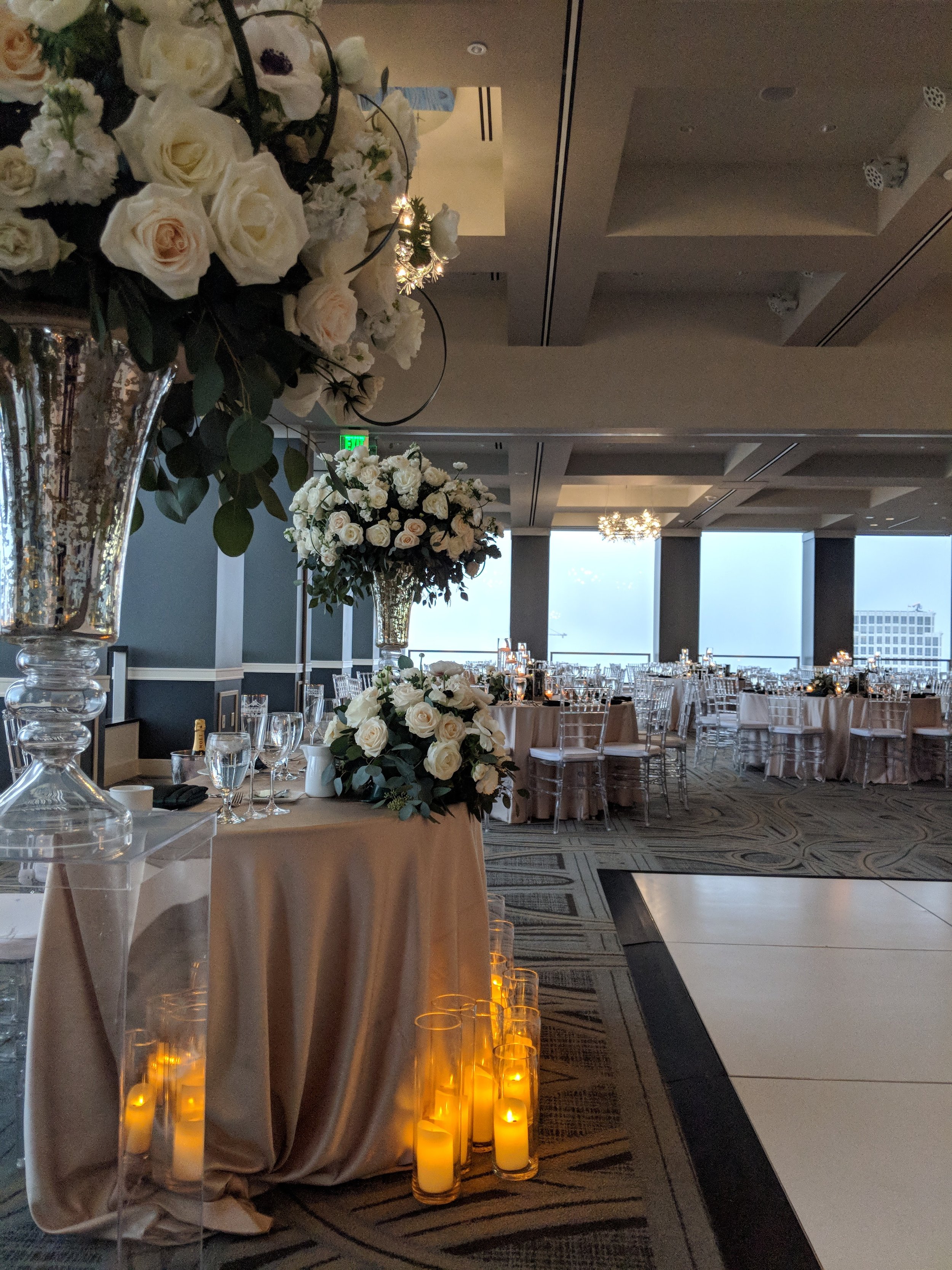 Elegant wedding reception venue with flower arrangements, candlelit ambiance, and round tables with chairs. Downtown LA - Interior Scapes Event Planning by Julie Jenkins