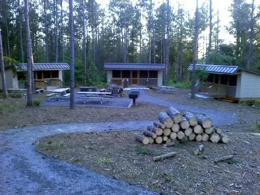 Three small wooden cabins in a wooded area with a pile of cut logs in the foreground. venues near me-local venues-interior scapes events by julie jenkins