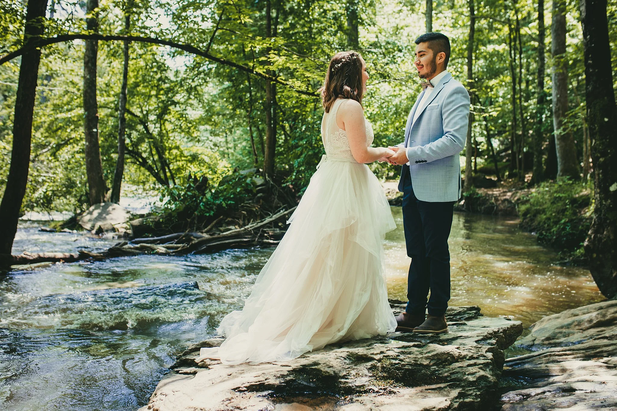 A bride and groom holding hands and exchanging vows on a large rock in a forested creek.   Sweetwater Creek State Park, Ga Interior Scapes Events by Julie Jenkins event planning