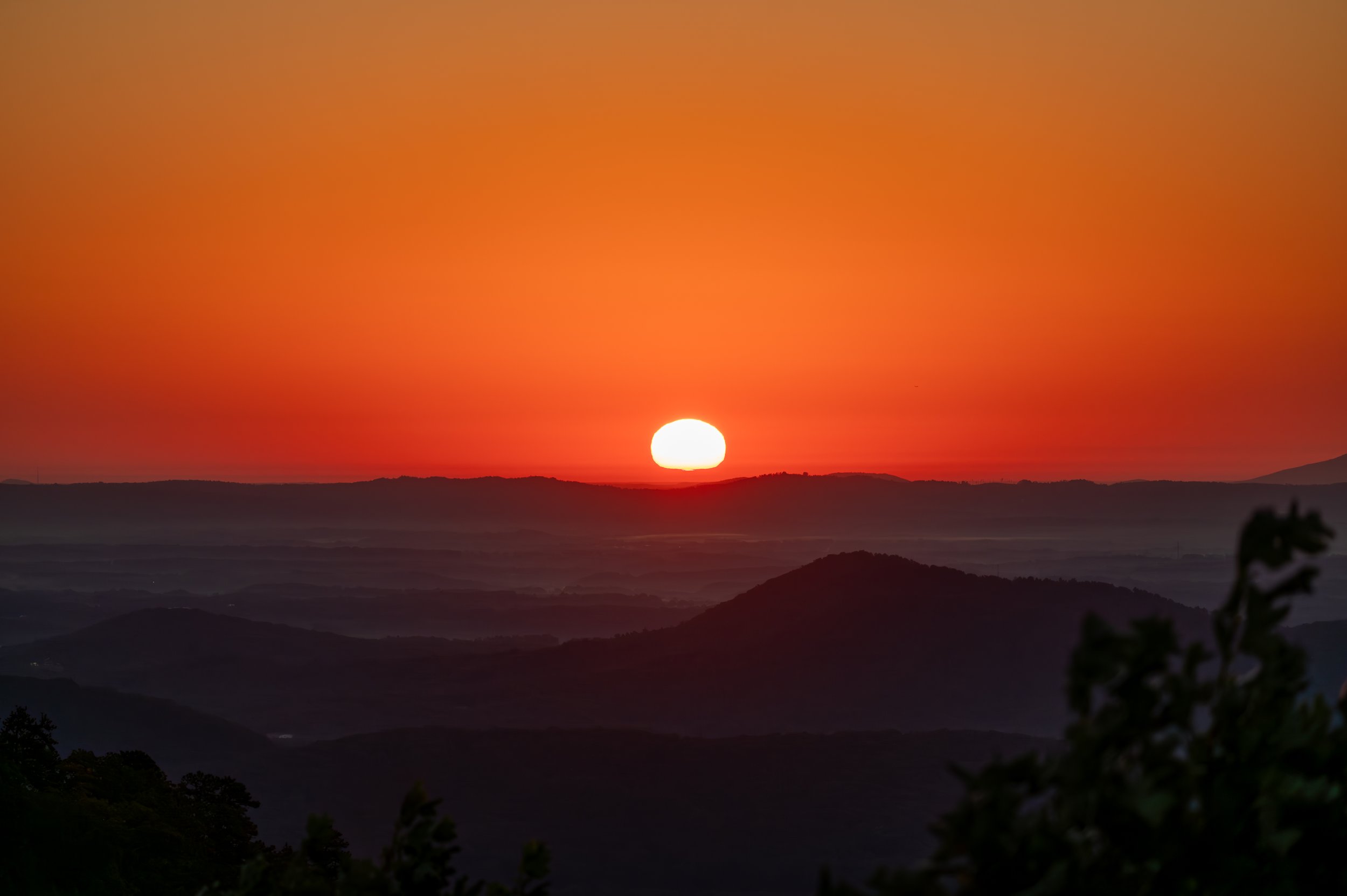 Sunrise over a mountainous Piedmont NC landscape with a bright orange sky and silhouetted hills in the foreground.