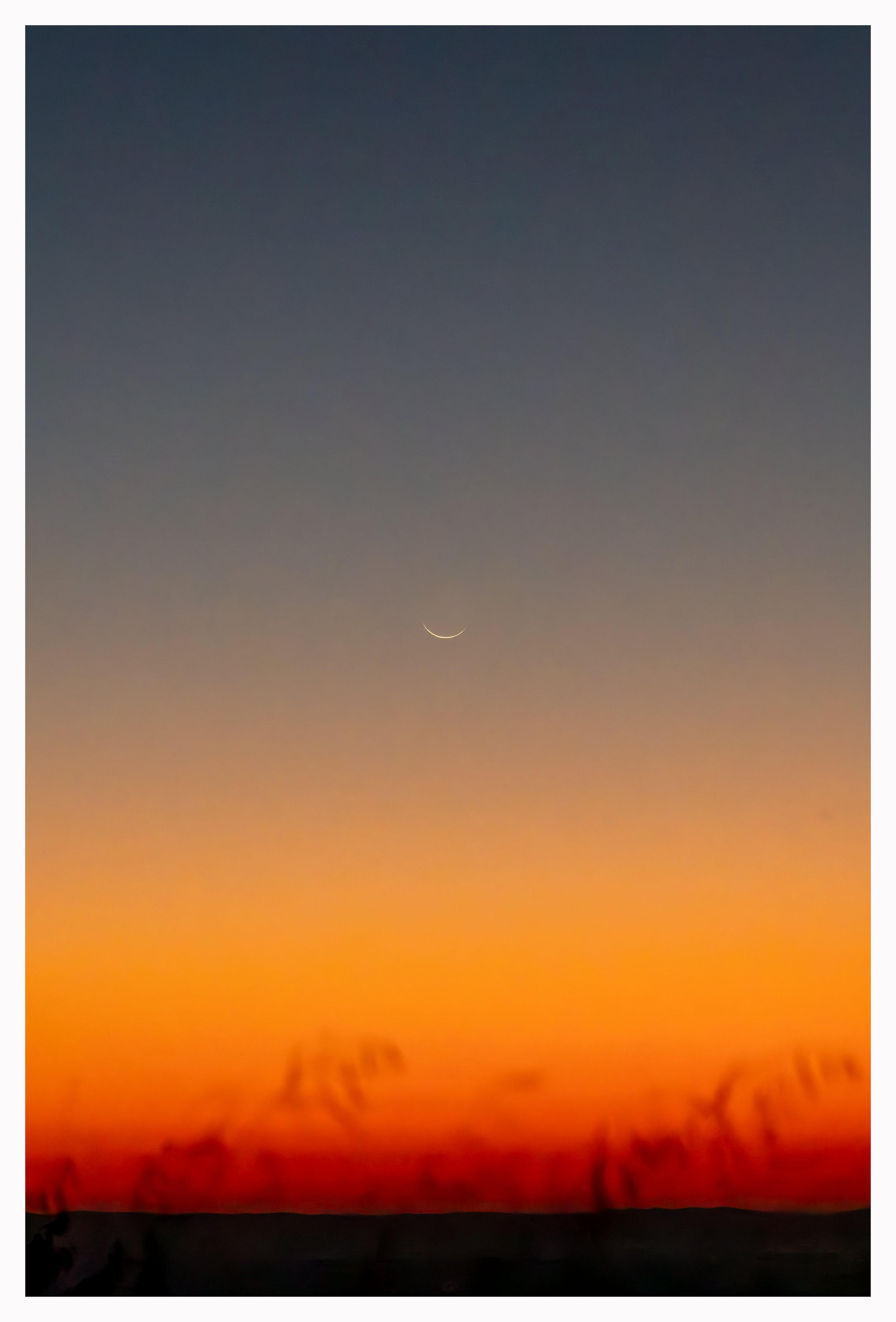 Crescent moon in a sunrise sky with gradient colors from orange to dark blue taken from the Blue Ridge Parkway