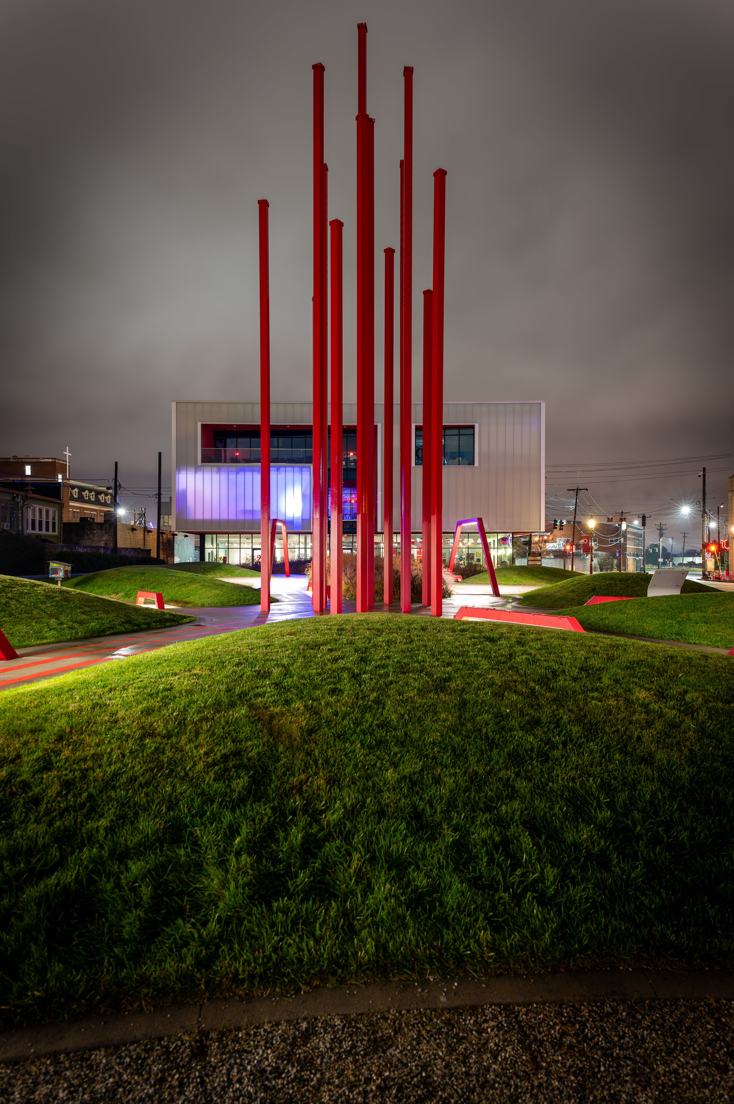 Night view of a modern building with tall red poles in front, surrounded by green grass and lit pathways.