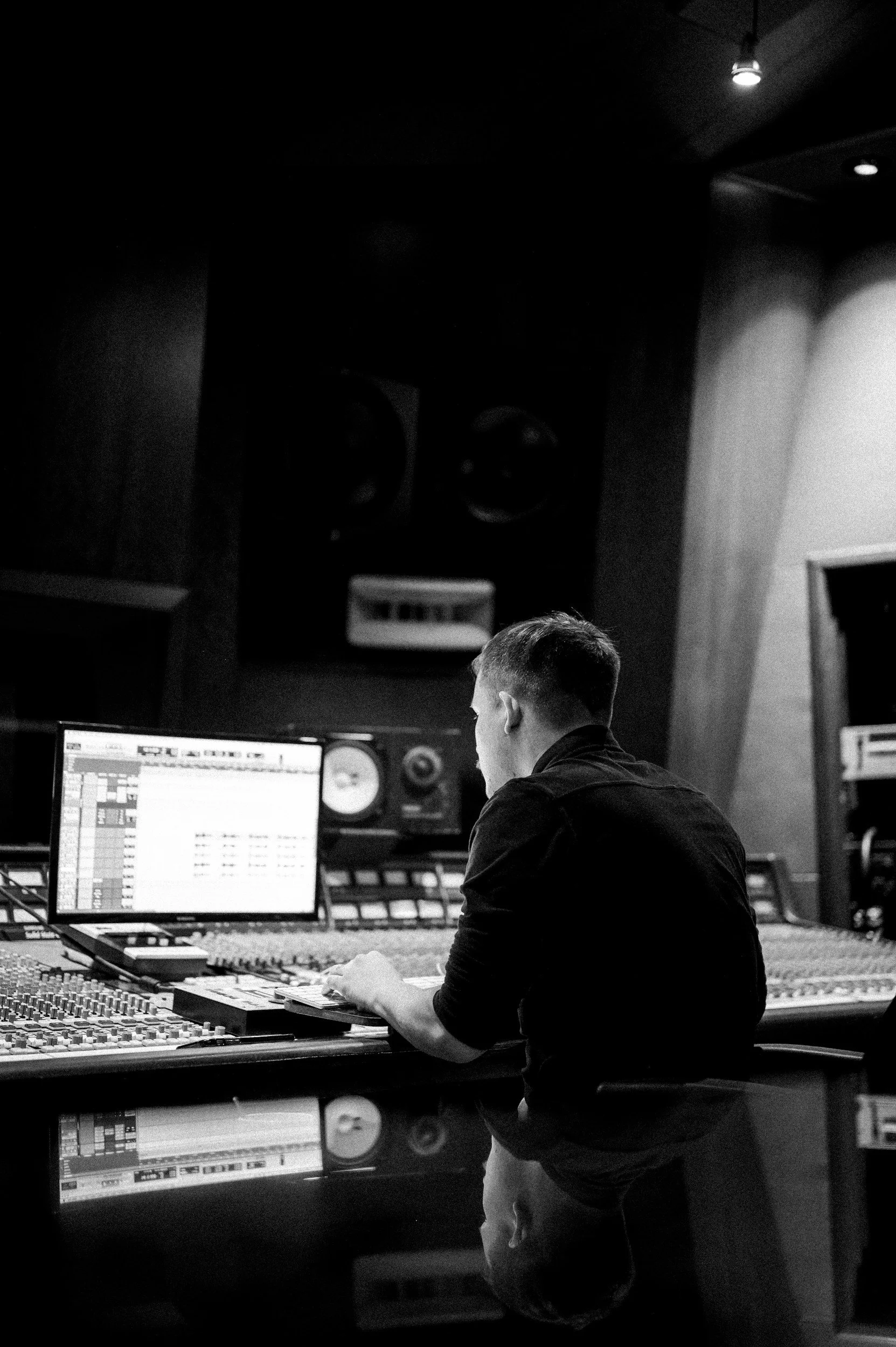 Une personne travaillant dans un studio d'enregistrement musical, assise devant une console de mixage et un ordinateur avec des enceintes