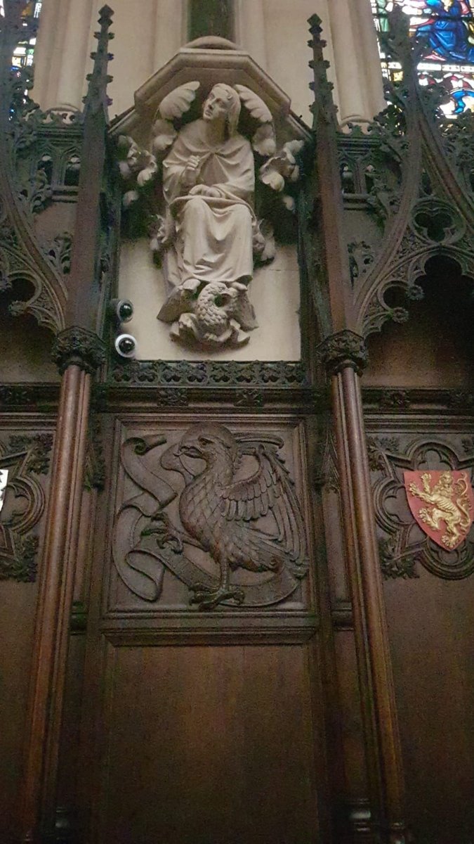 A carved stone religious sculpture of Jesus Christ seated, with a dog at his feet, set in a gothic cathedral with stained glass windows and wood paneling featuring a griffin emblem.