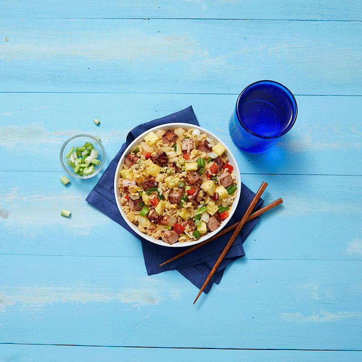 Stop motion GIF of bowl of chicken fried rice with vegetables, glass of water, and chopsticks on a blue wooden table.