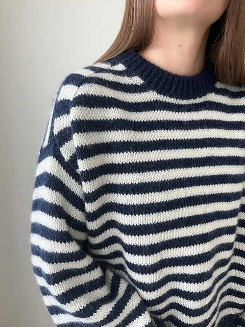 Close-up of a person wearing a navy blue and white striped knit sweater, with part of their face and shoulder visible.