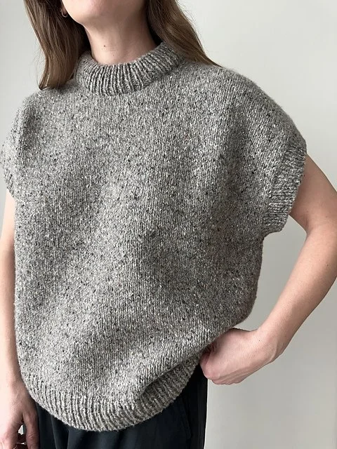 Person wearing a sleeveless gray knit sweater with a high neckline, standing against a plain background.