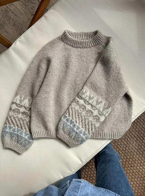 A cozy knit sweater with a snowflake pattern on the sleeves, placed on a white table.