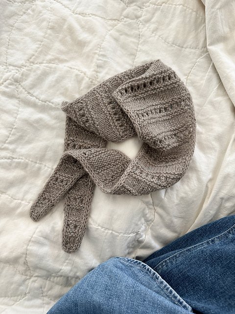 A gray knitted scarf and hat lying on a white quilted surface.