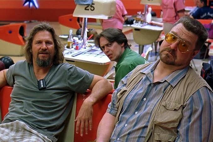 Three men sitting in a bowling alley, with bowling lanes and other people in the background.