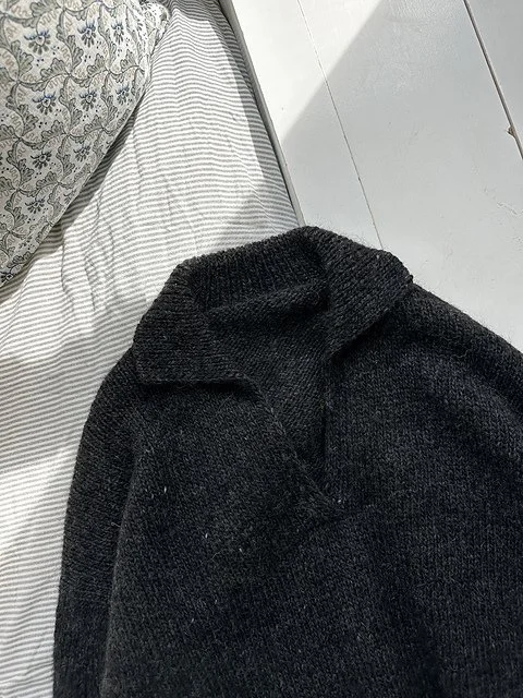 Close-up of a black sweater on a bed with white and striped sheets and a patterned pillow