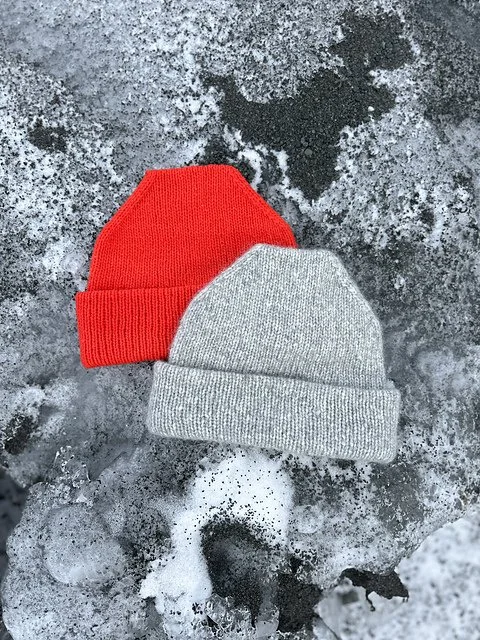 Red and gray knit beanies on snow-covered ice, with a small tree stick nearby.