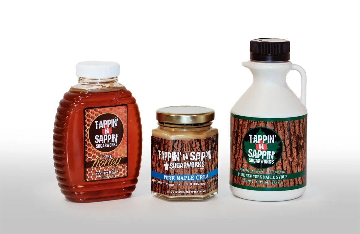 Three jars of syrup and cream with labels reading 'Tappin' N Sappin' Sugarworks' and 'Pure Maple Cream' and 'Pure New York Maple Syrup'.