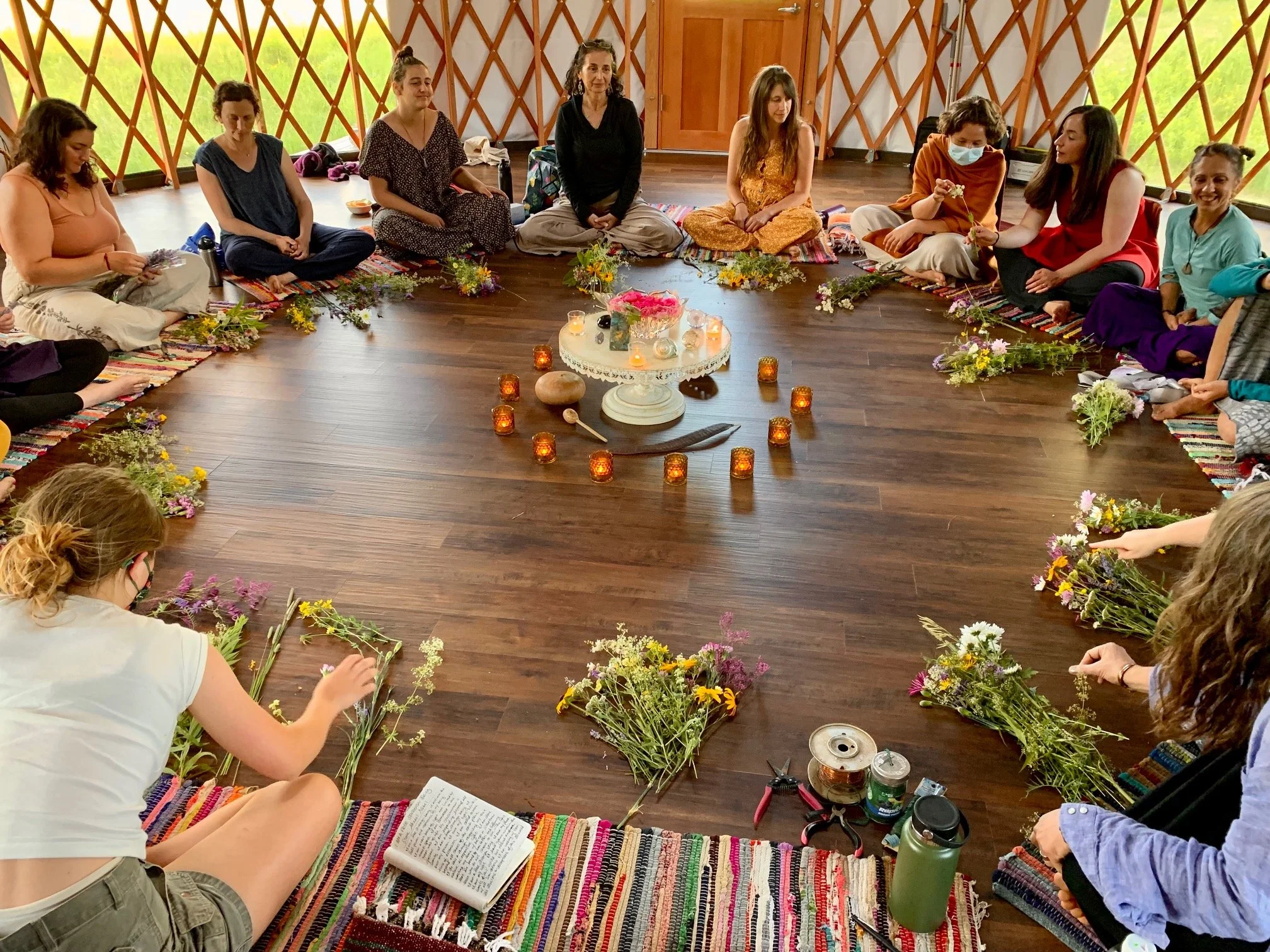 Women gathered in a circle with flowers inside of a yurt.