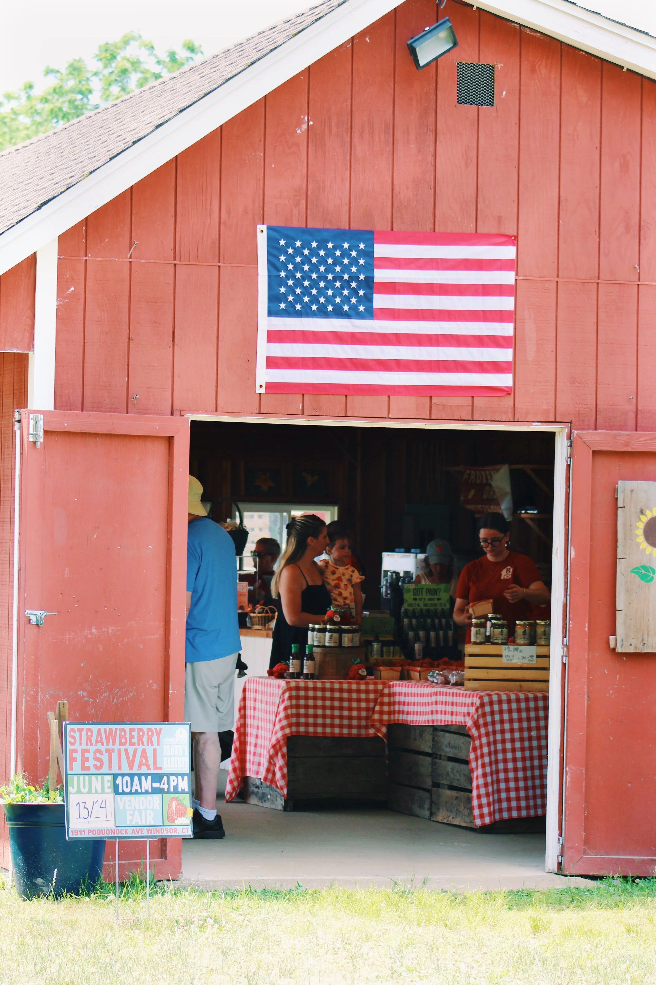 People at a strawberry festival selling fresh strawberries at a stand in a red barn with an American flag hanging on the wall.