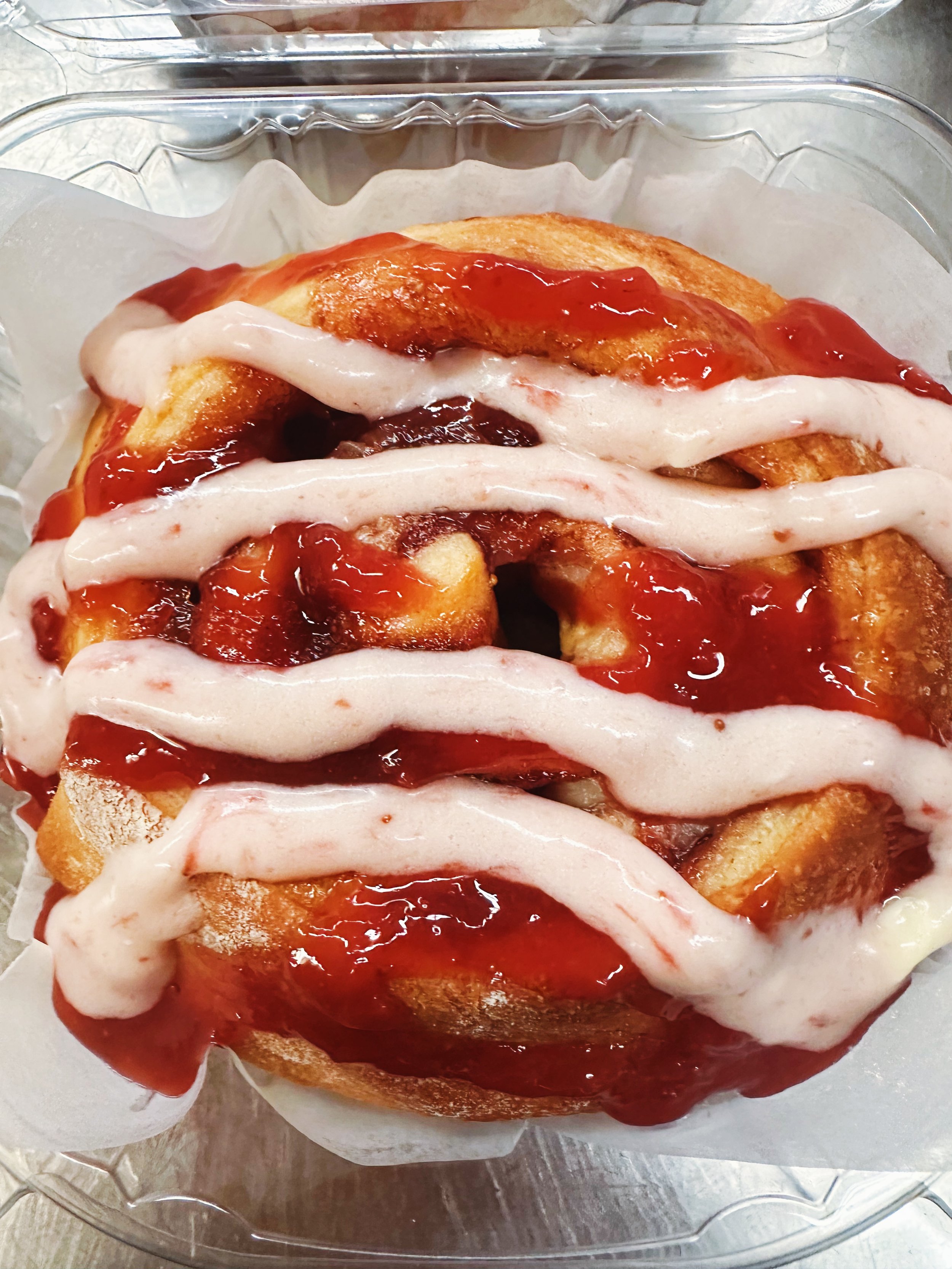 A decorative cake with purple and orange frosting and drizzled with red sauce, topped with whipped cream, served in a clear glass dish lined with parchment paper.