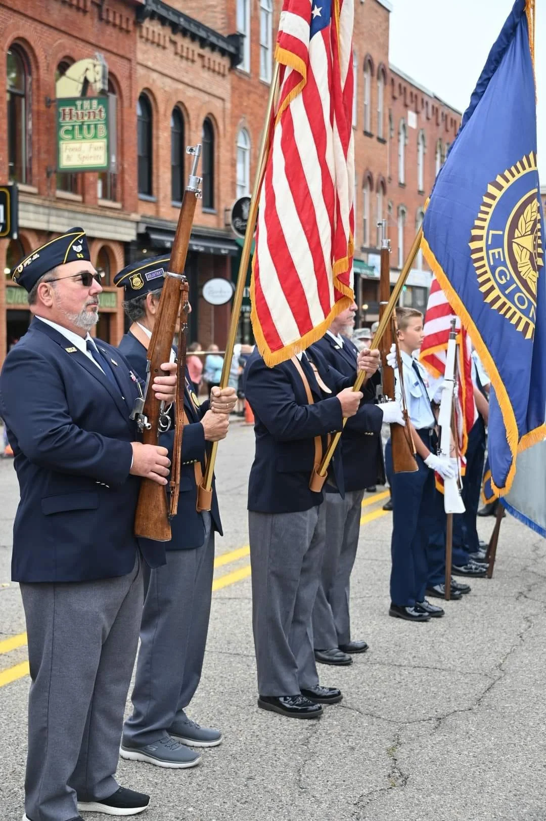 Members of a color guard dressed in vintage military uniforms holding American flags and a Veterans of Foreign Wars flag during a parade.