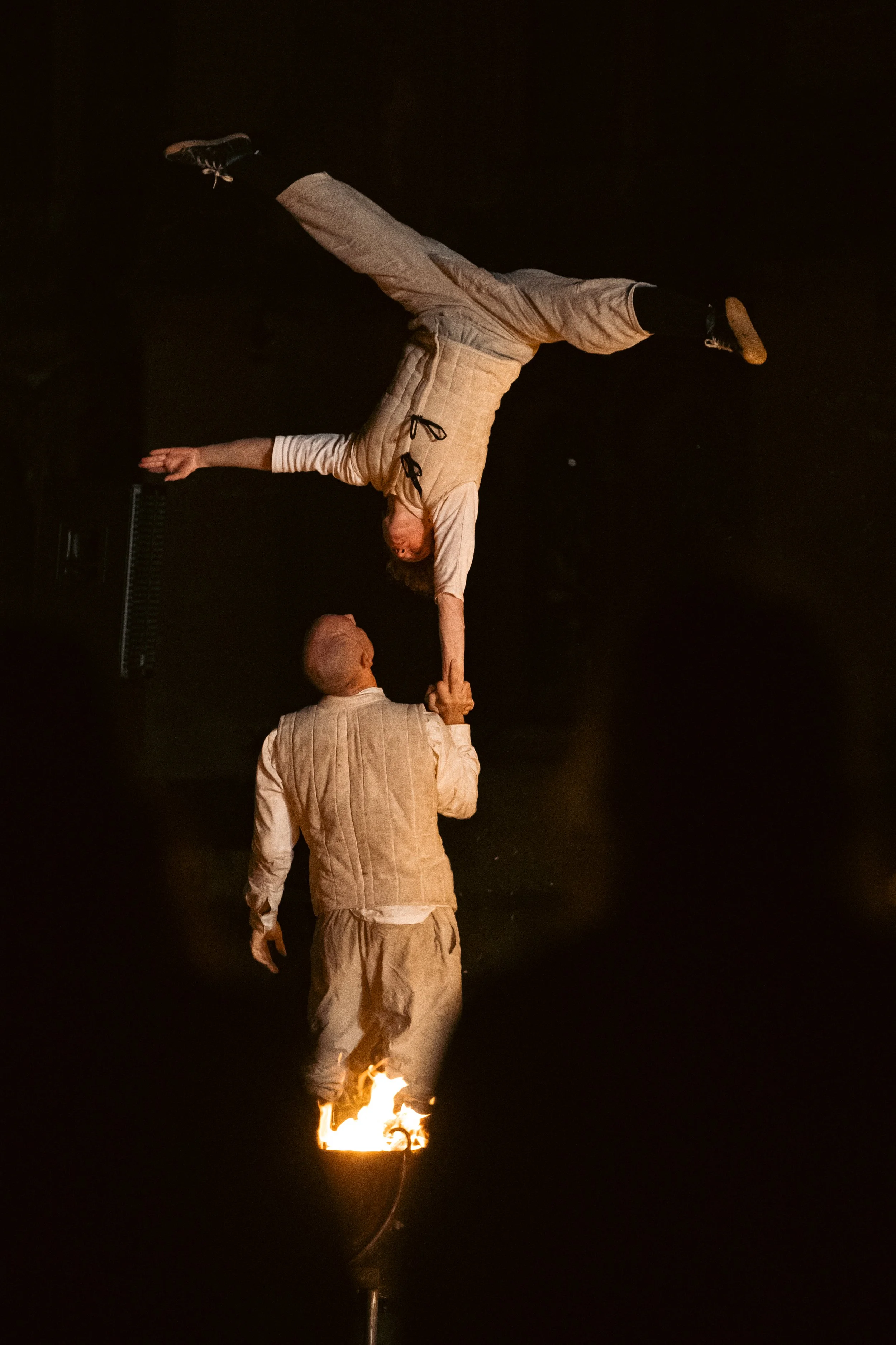 Two performers, one standing and one upside down, on a stage with a flaming torch. Nikki & JD Fireside
