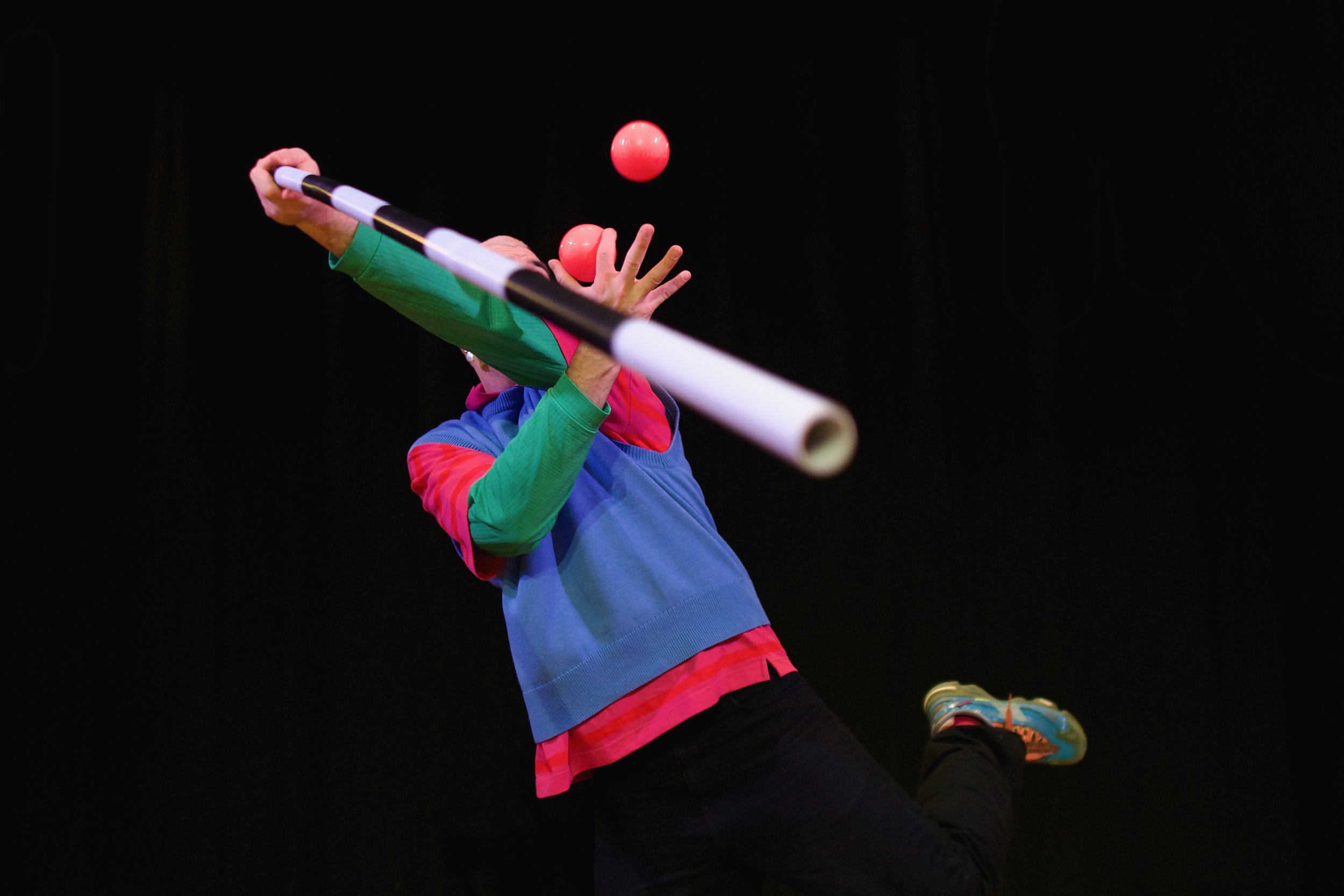 Child in colorful clothing catching a red ball with a bat