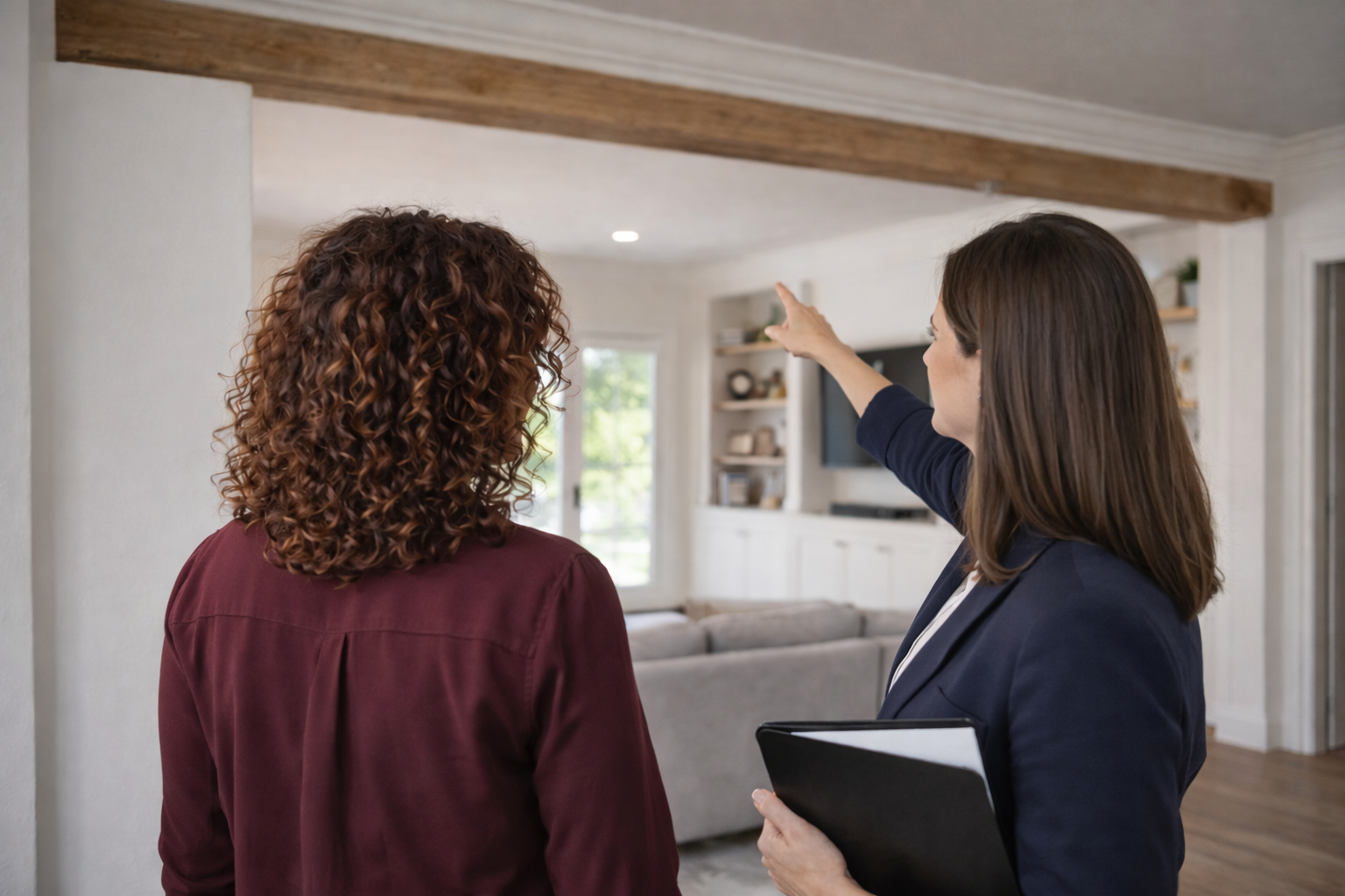 Real estate agent showing a house to a client, pointing towards the ceiling or wall.