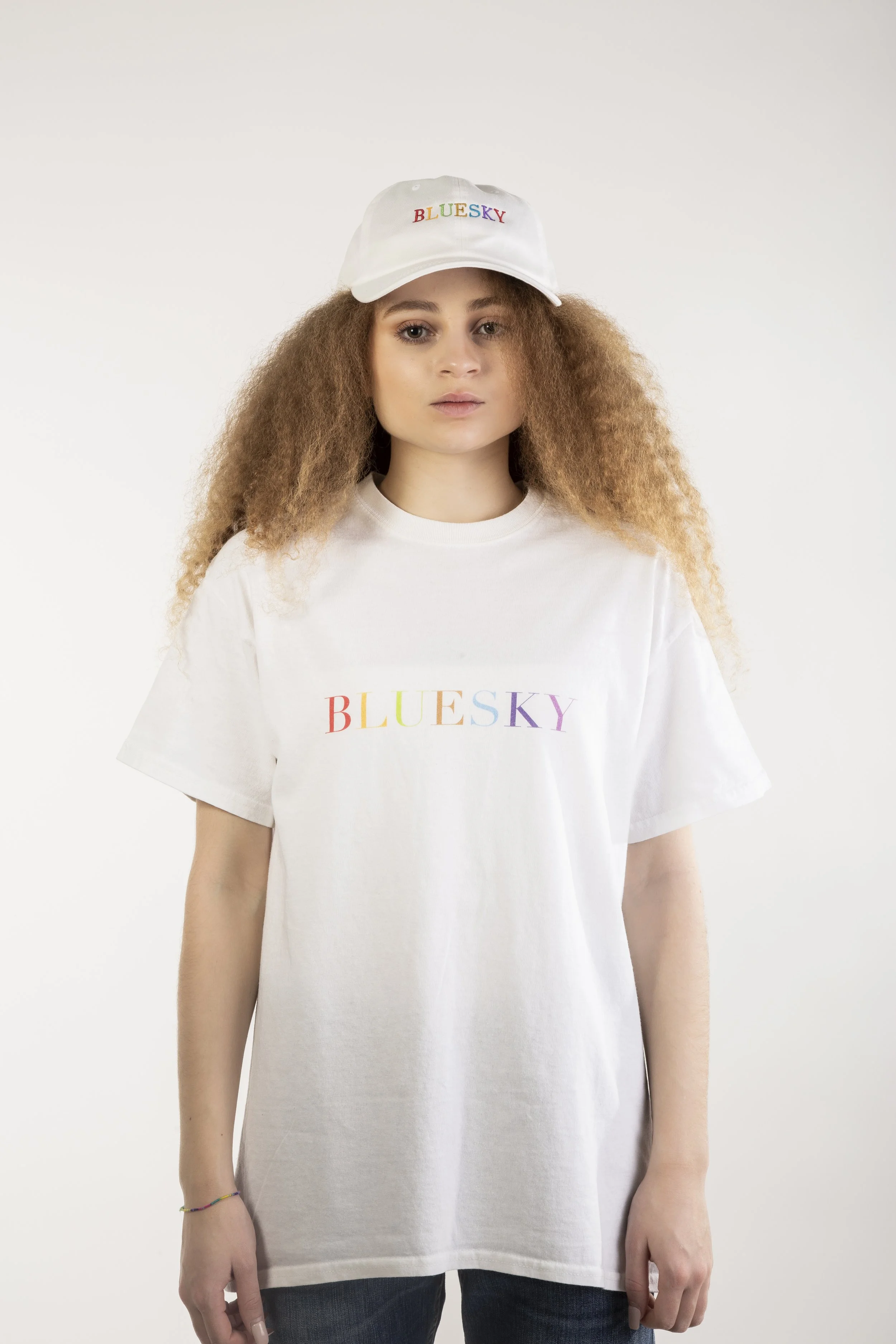 Jeune femme portant un t-shirt blanc et une casquette blanche, tous deux avec le texte "BLUESKY" en lettres colorées.