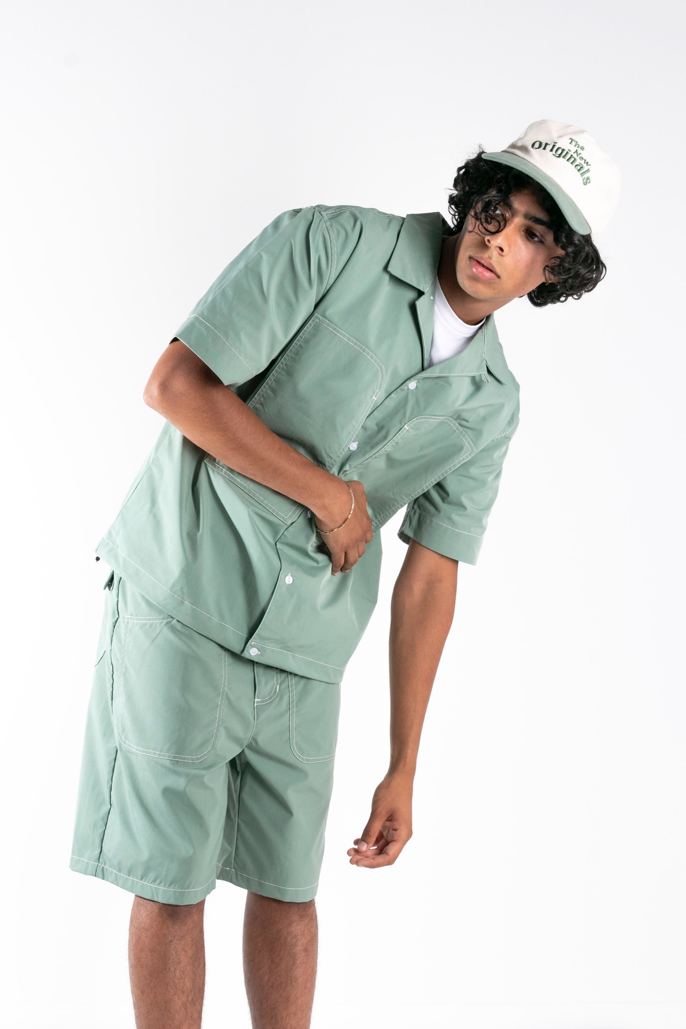 Jeune homme portant un ensemble vert avec un chapeau blanc.