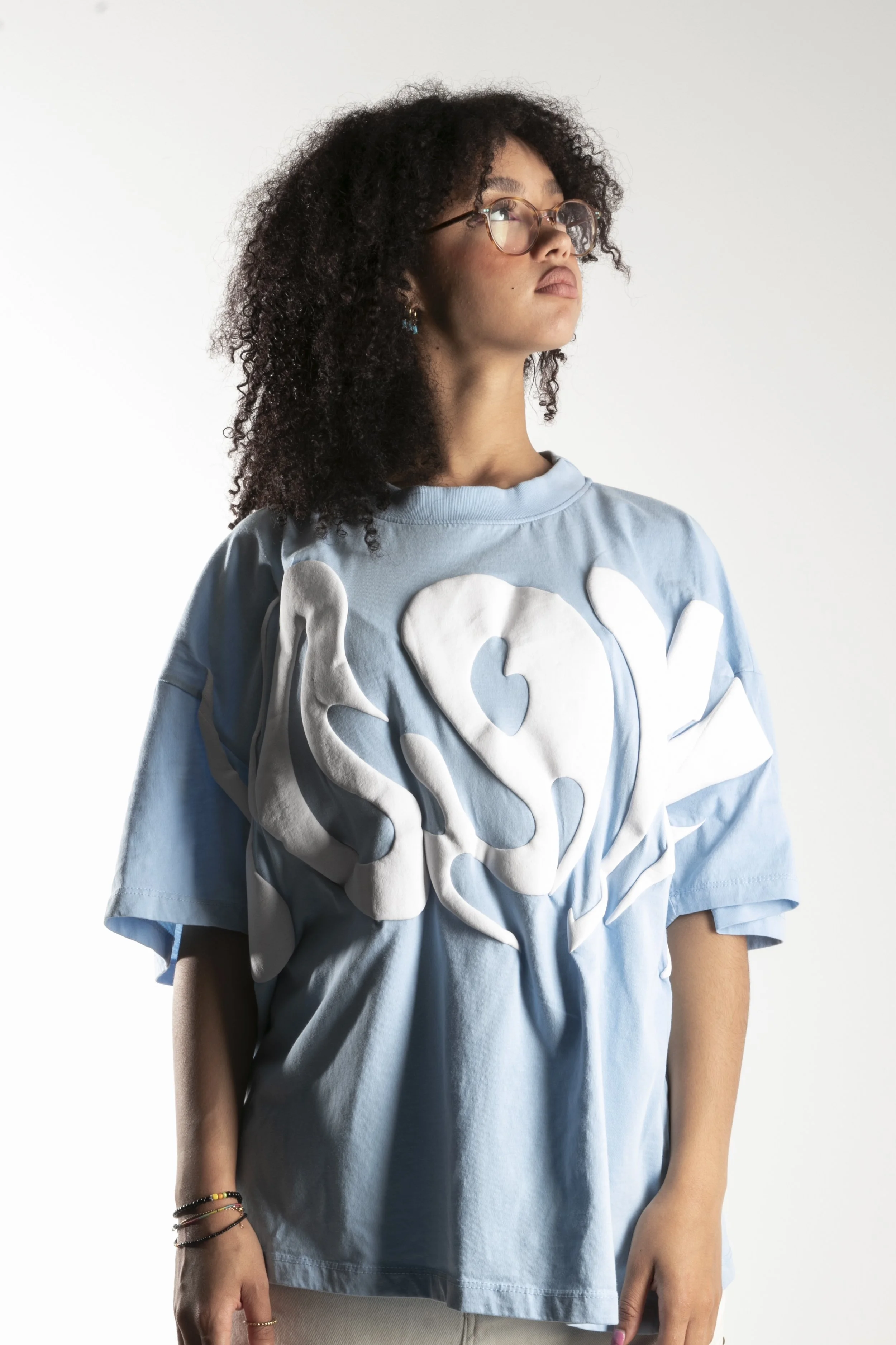 Jeune femme portant un sweat-shirt bleu clair avec un grand motif blanc en relief au centre, fond blanc
