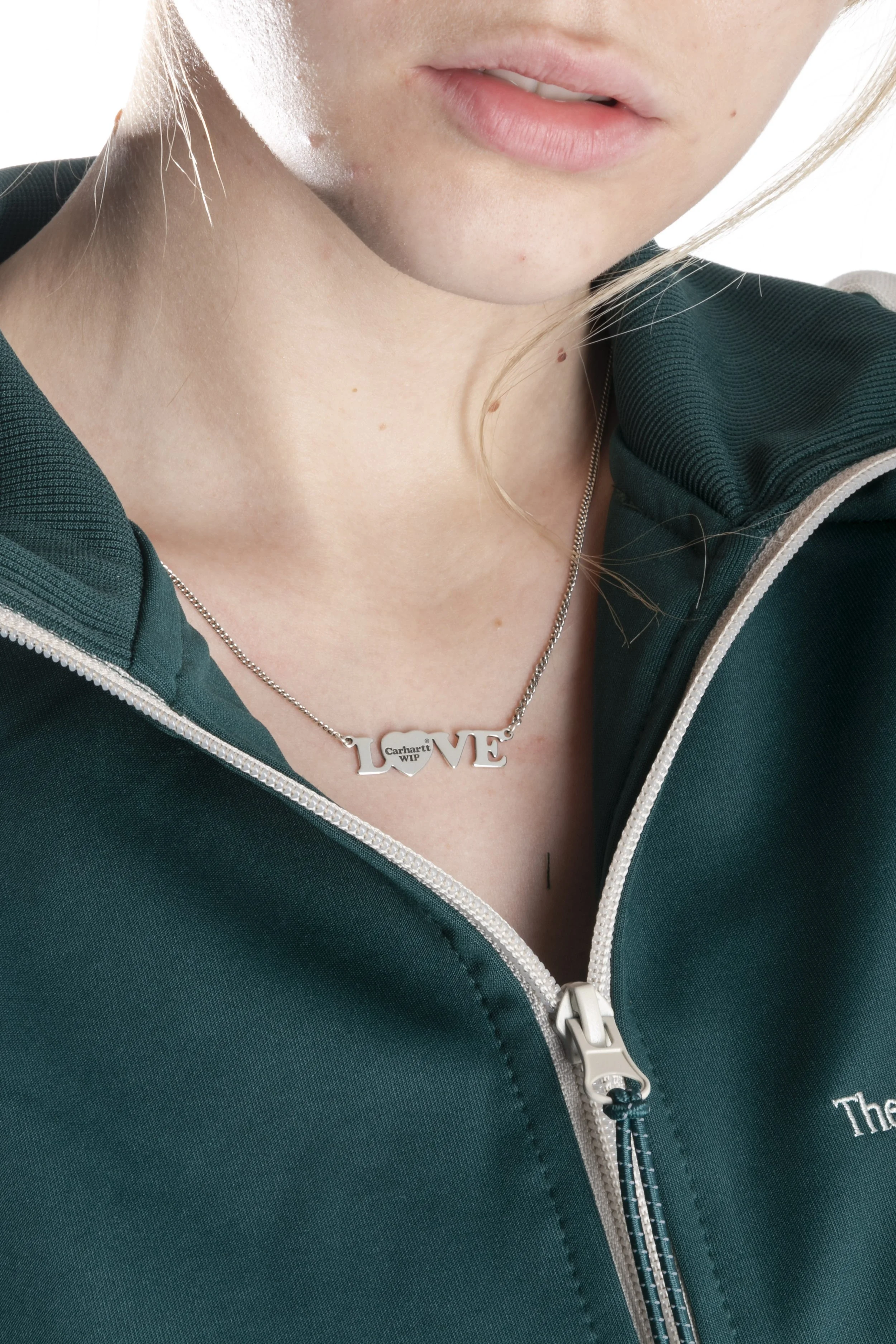 Collier avec le mot 'LOVE' porté par une personne portant une veste verte à zip.