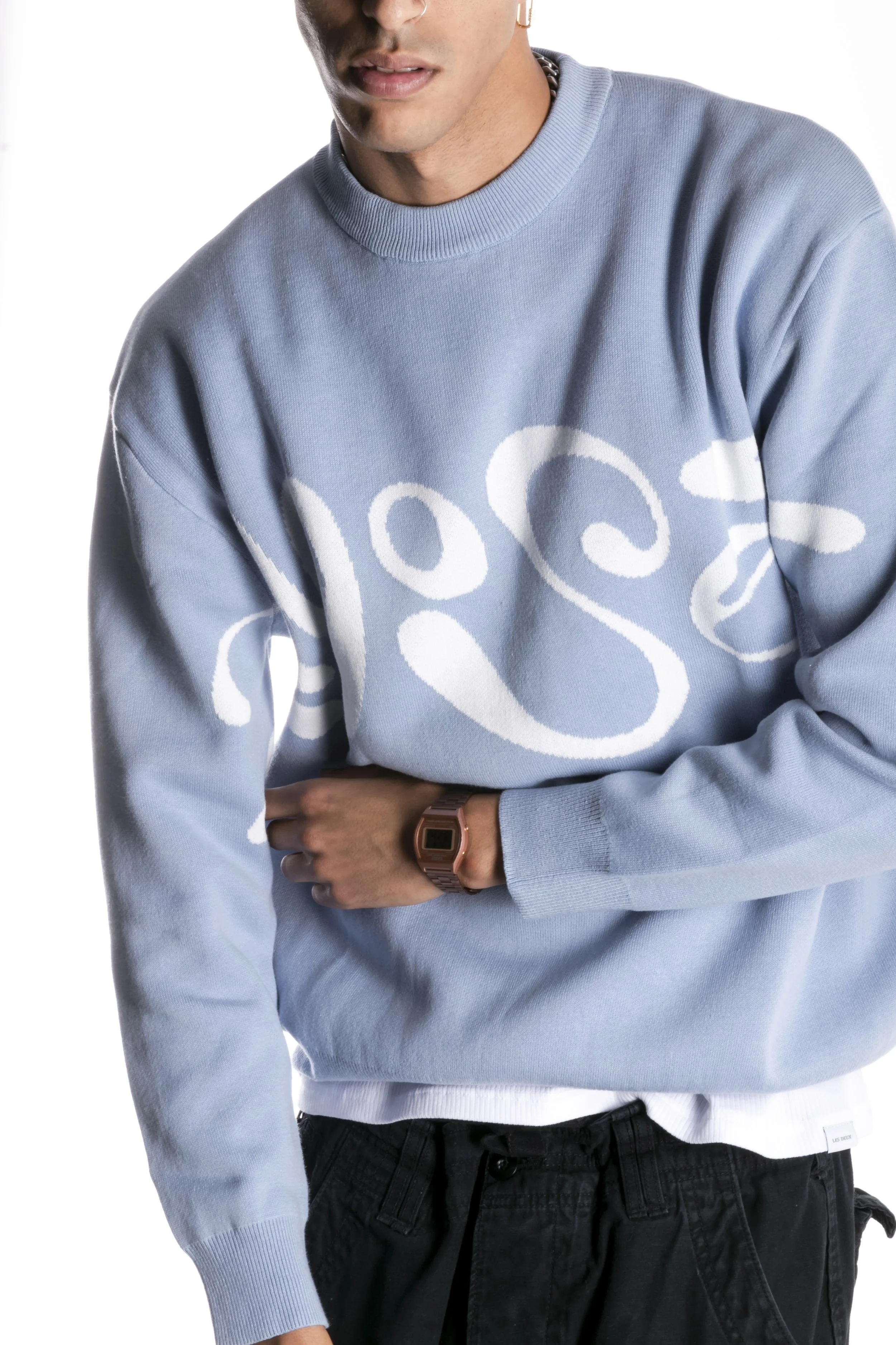 Homme portant un sweat-shirt bleu clair avec un dessin blanc de spirales et un bracelet rose en métal.