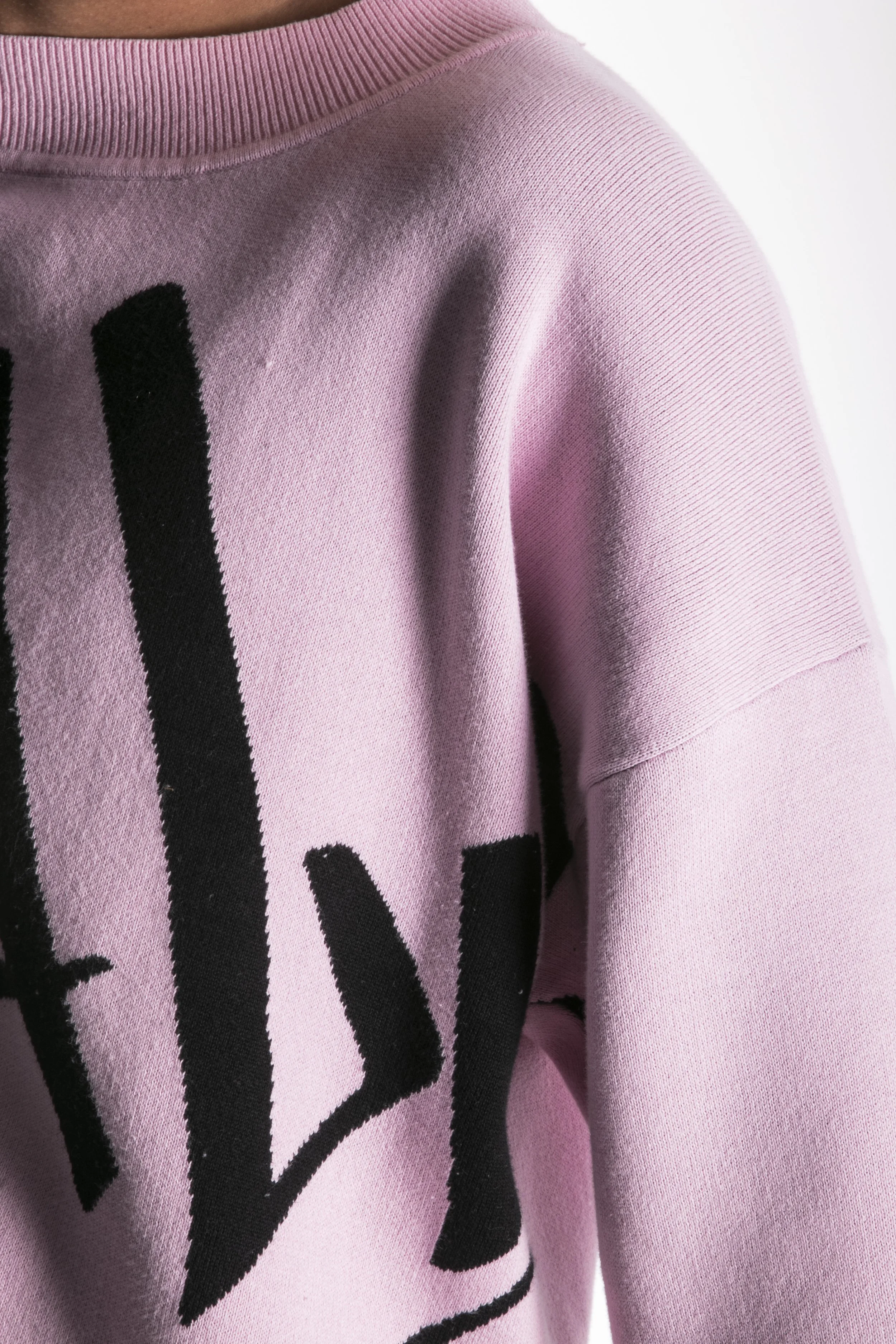 Partie supérieure d'un pull rose avec des lettres noires imprimées, montrant l'épaule et le col