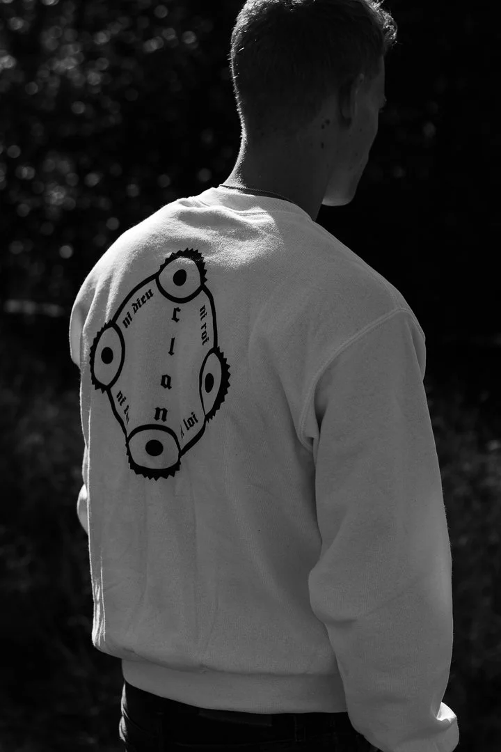 Jeune homme vu de dos portant un sweat avec un logo circulaire sur le dos, en extérieur