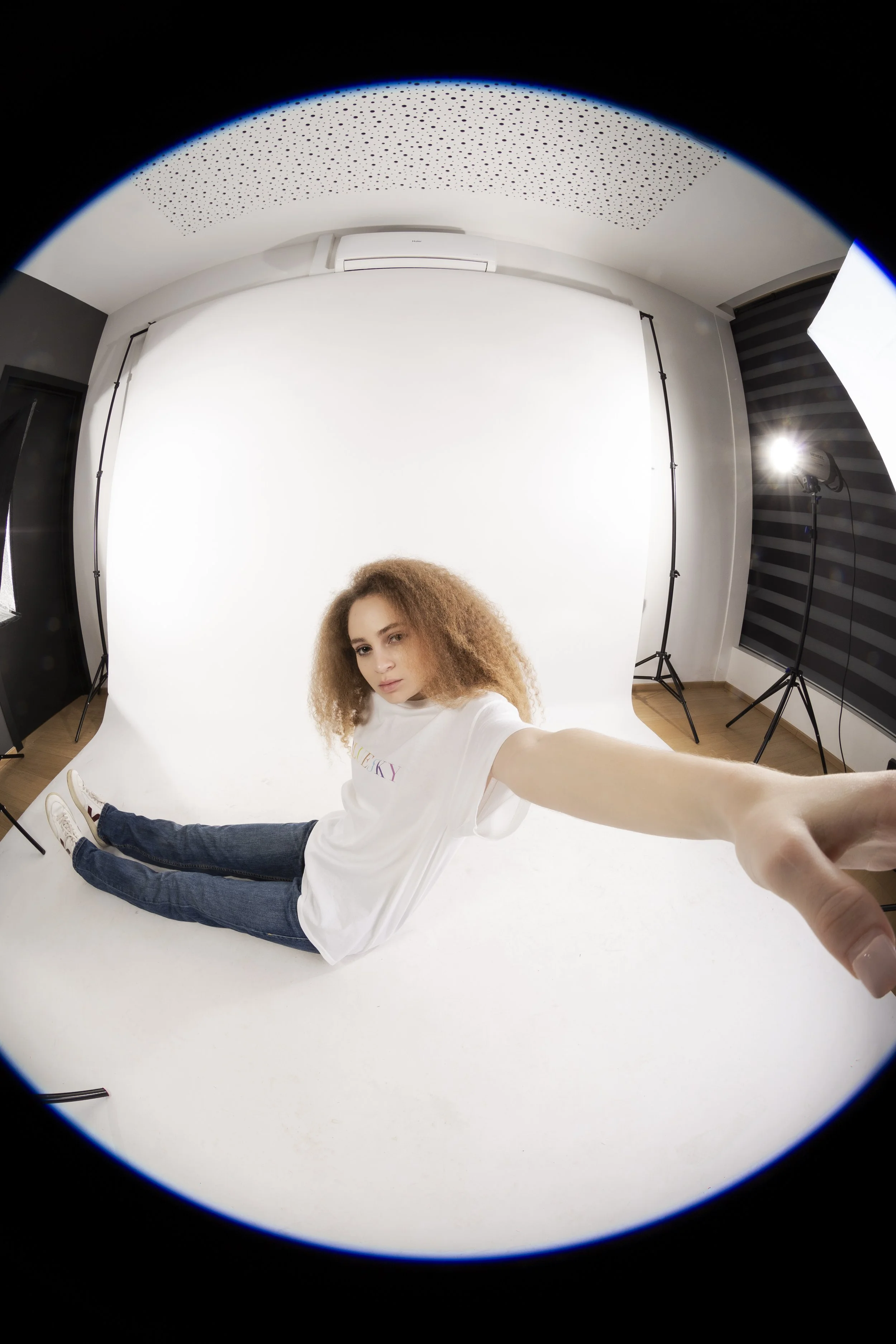 Jeune femme assise sur un fond blanc dans un studio de photographie, prise de vue en fisheye