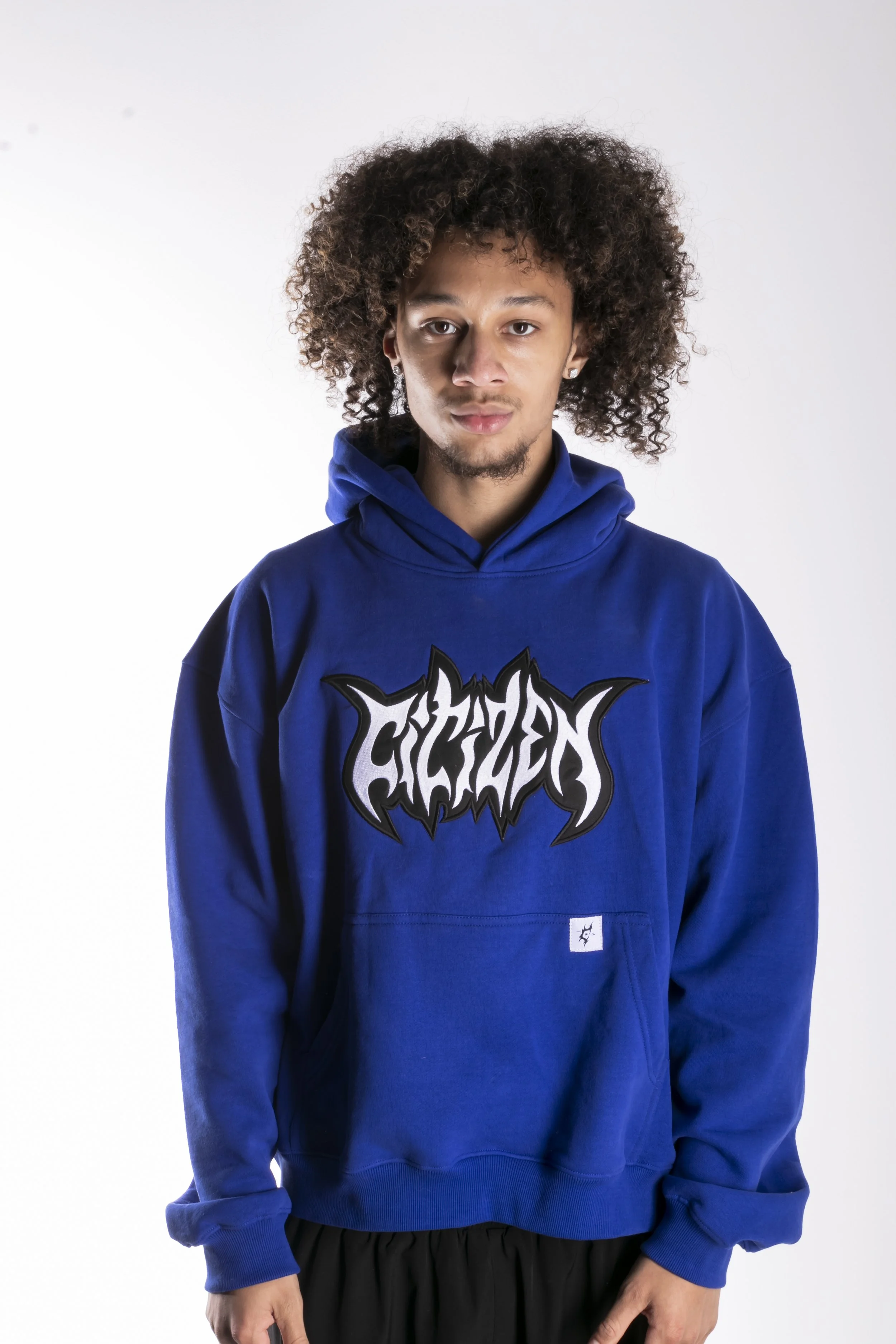 Jeune homme portant un sweat à capuche bleu avec un logo graphique blanc et noir, debout devant un fond blanc.