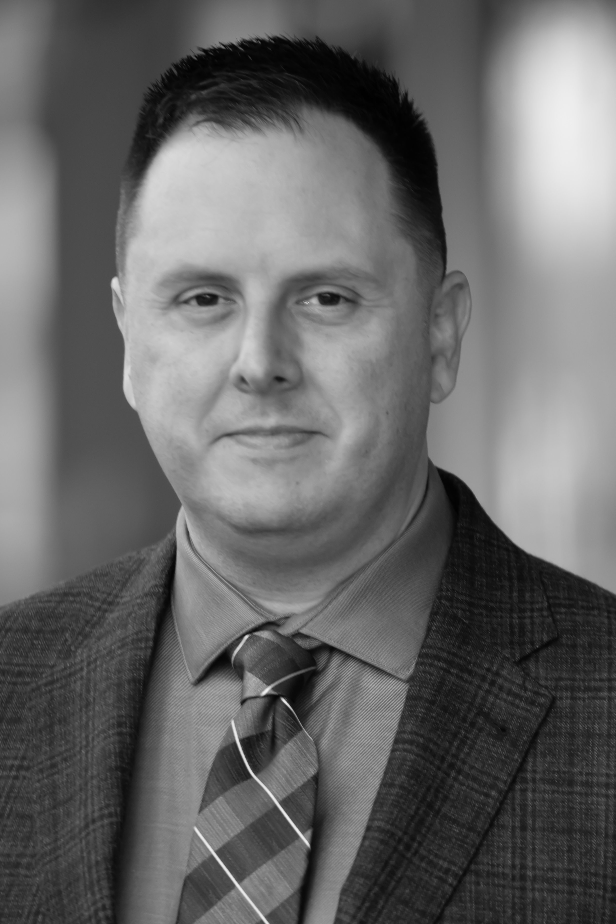 Black and white portrait of a man in a suit and tie, looking at the camera with a slight smile.