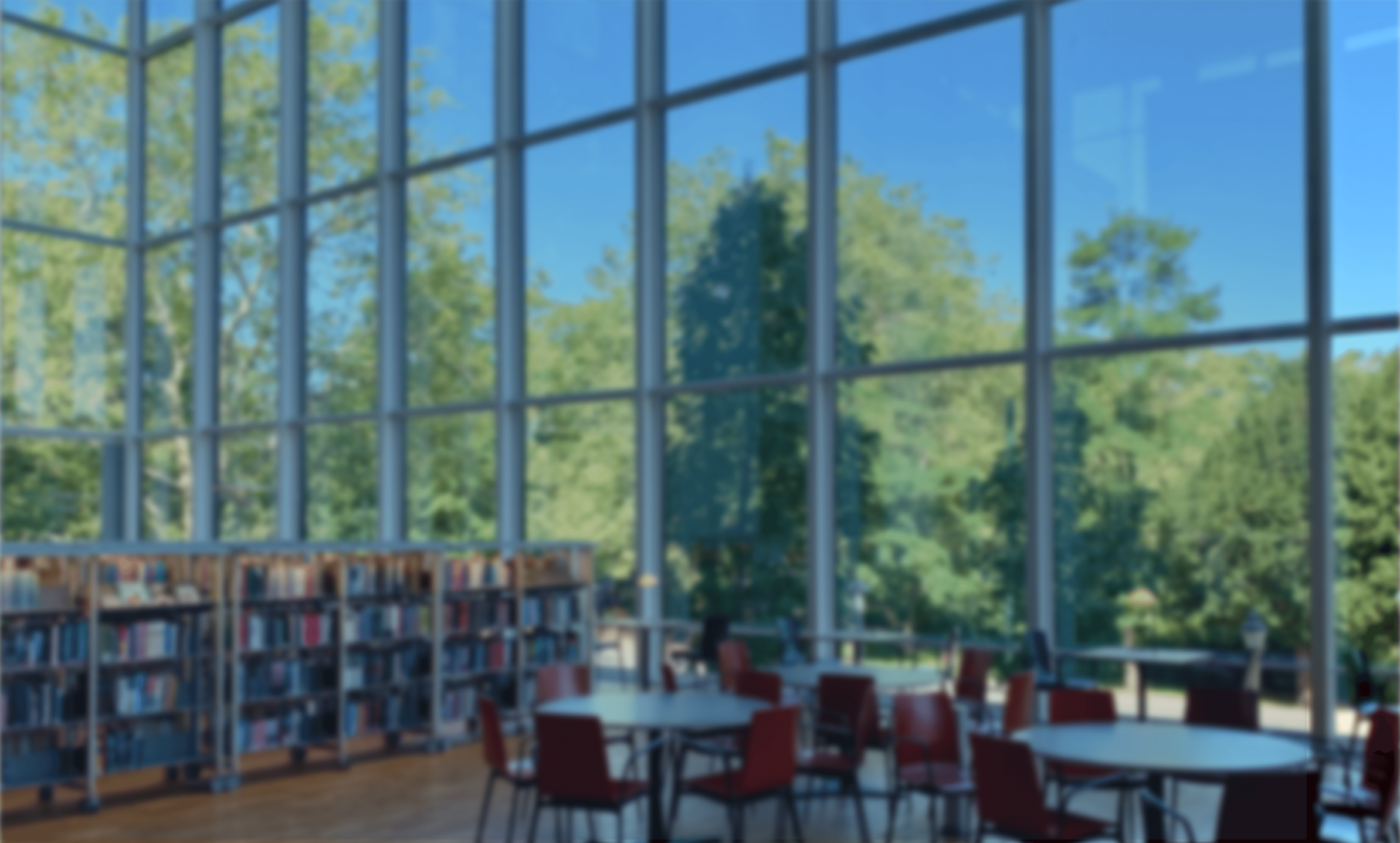 Interior of a modern library with large glass windows showing trees outside, bookshelves, tables, and red chairs.