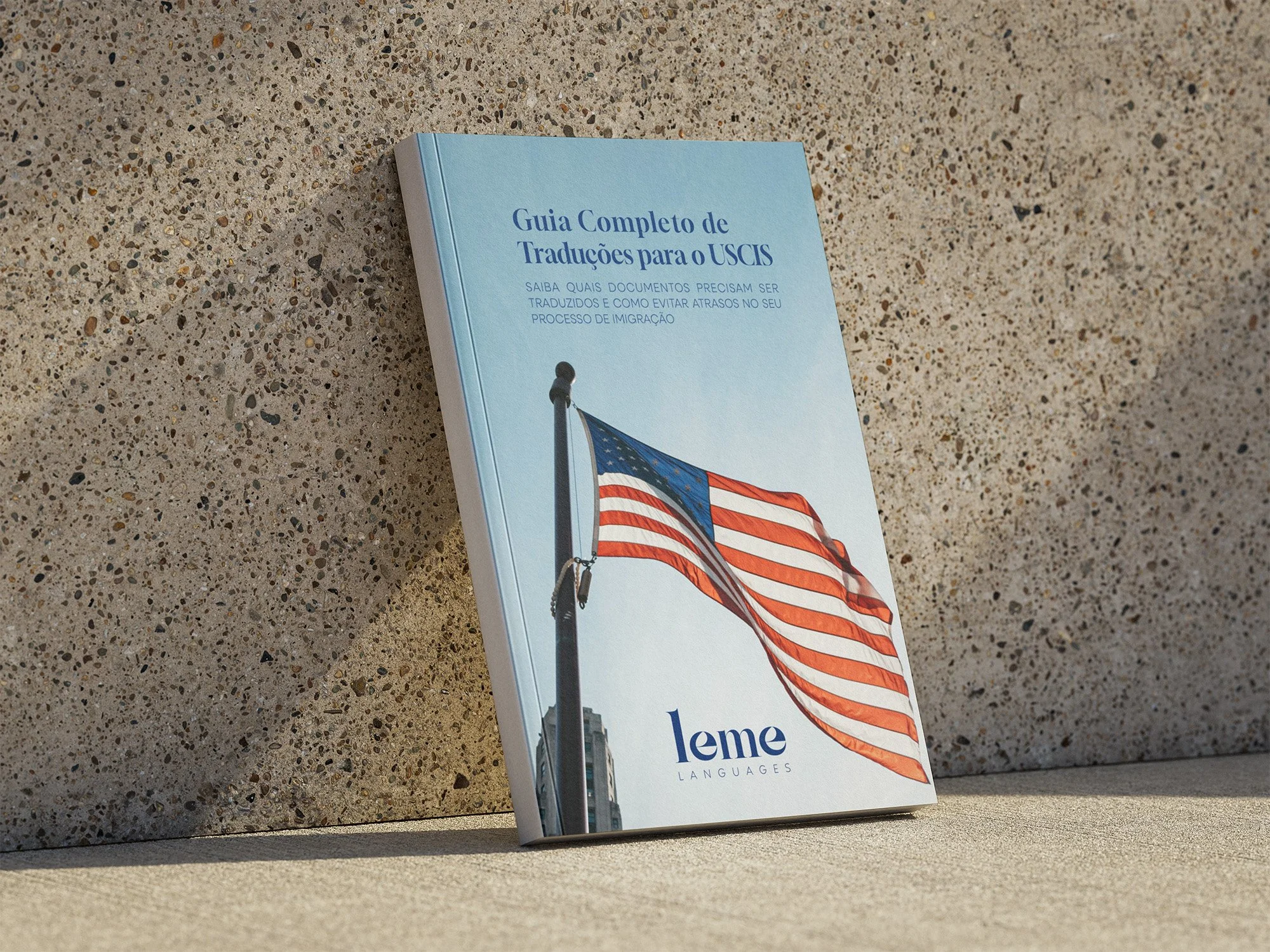 A book titled 'Guia Completo de Traduções para o USCIS' with an American flag on the cover, resting against a textured wall.