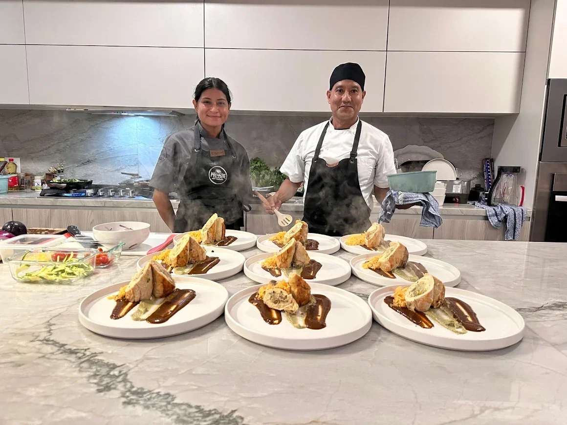 Chef and sous-chef standing behind a marble kitchen island with plated dishes of bread, sauce, and garnish, ready to serve.