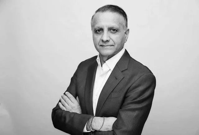 Black and white portrait of a man in a suit with arms crossed, standing against a plain background.