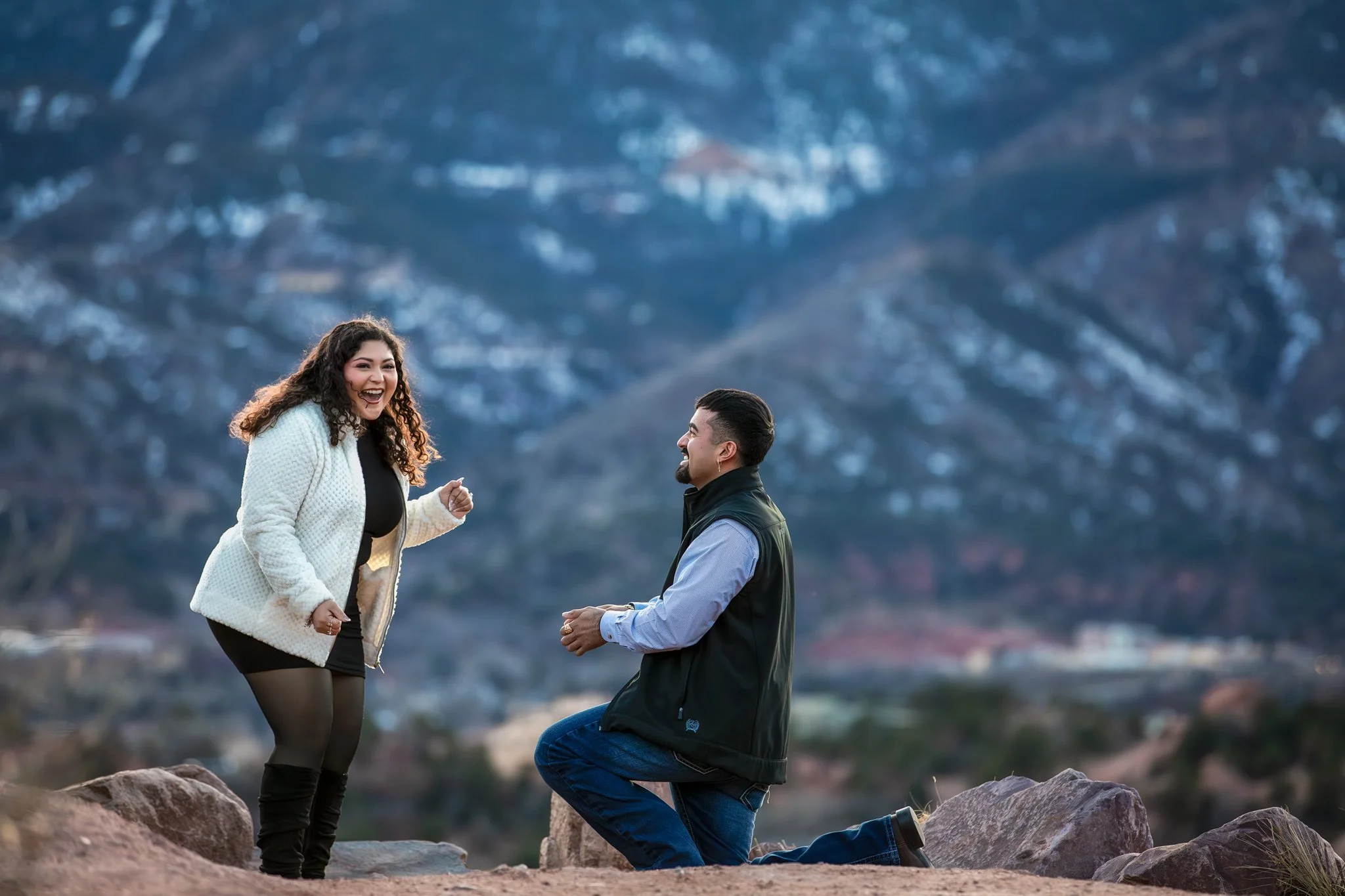 A man proposed to a woman in a mountainous outdoor setting, with both of them smiling and happy.