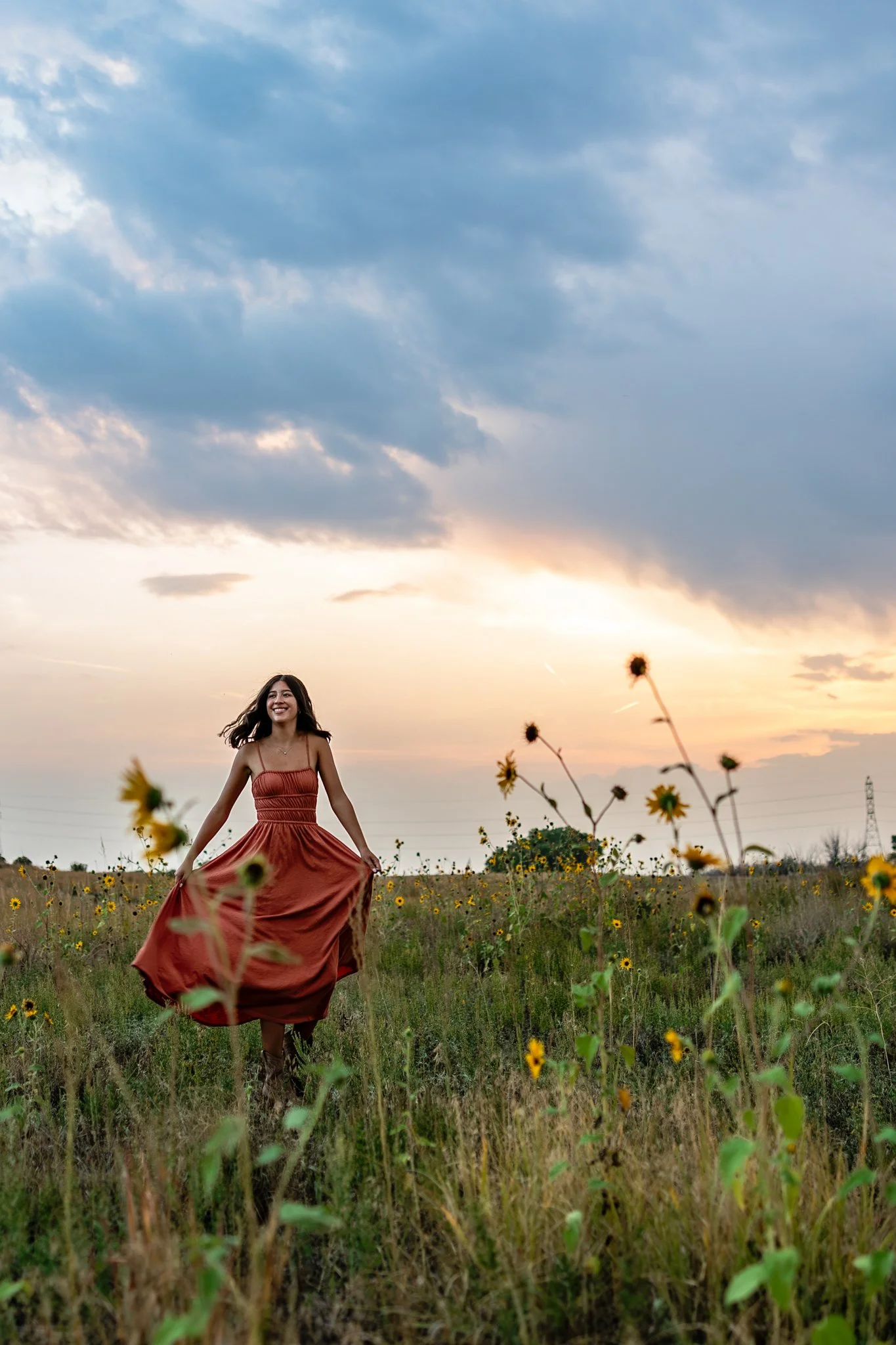 Denver Colorado Senior Photographer captures a high school senior girl in a muted red dress spinning in a field of sunflowers at sunset.