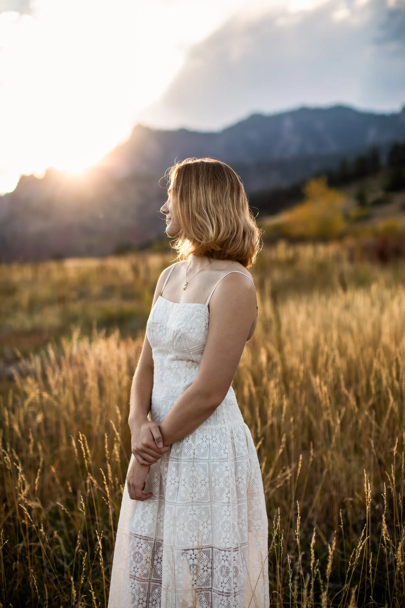 Colorado senior portrait photographer captures photograph of girl with short blonde hair and transparent white dress staring into a golden field at sunset