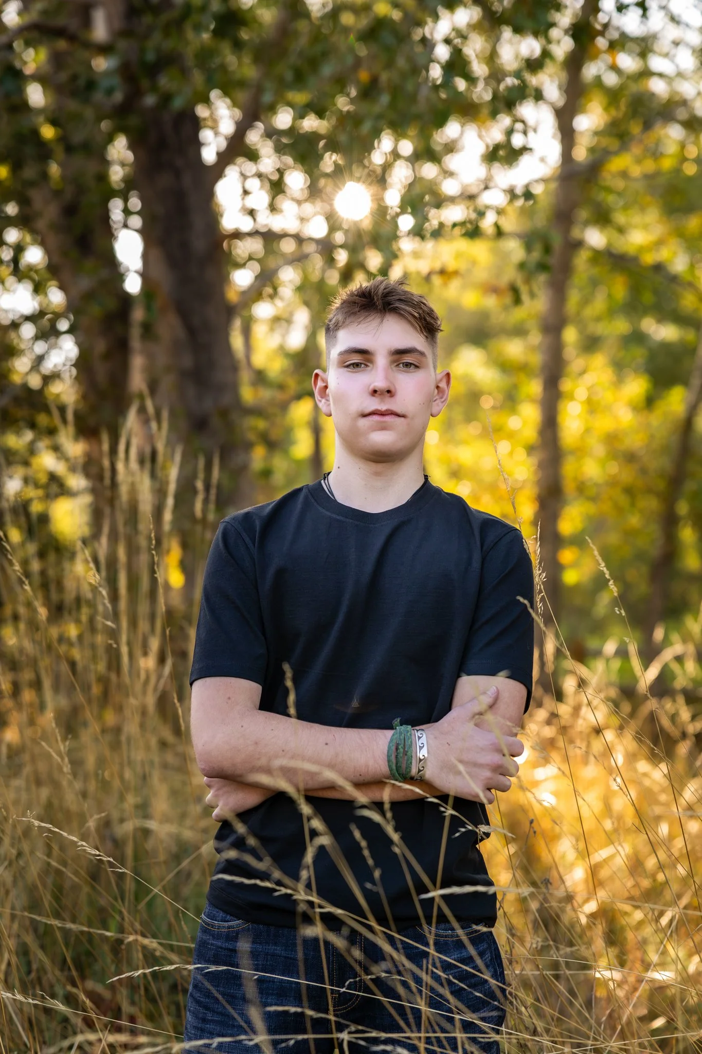 High School Senior Photographer takes a picture of a young man with his arms crossed wearing a black tshirt.