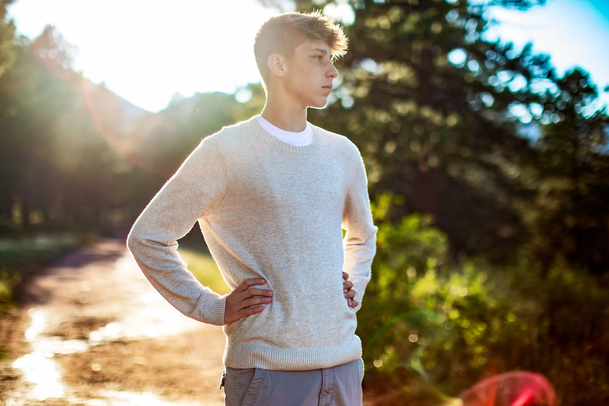 Portrait of a teenage boy with his hands on his hips looking off into the distance on a trail in Boulder Colorado.