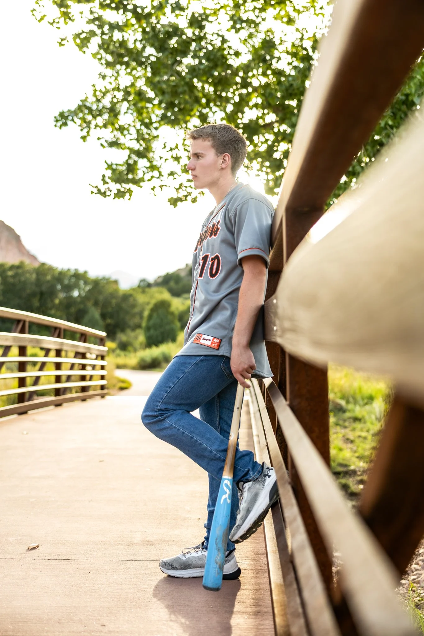 Colorado Springs Senior Photographer captures photograph of a high school senior boy on a bridge at Garden of the Gods dressed in his baseball jersey and holding a baseball bat.