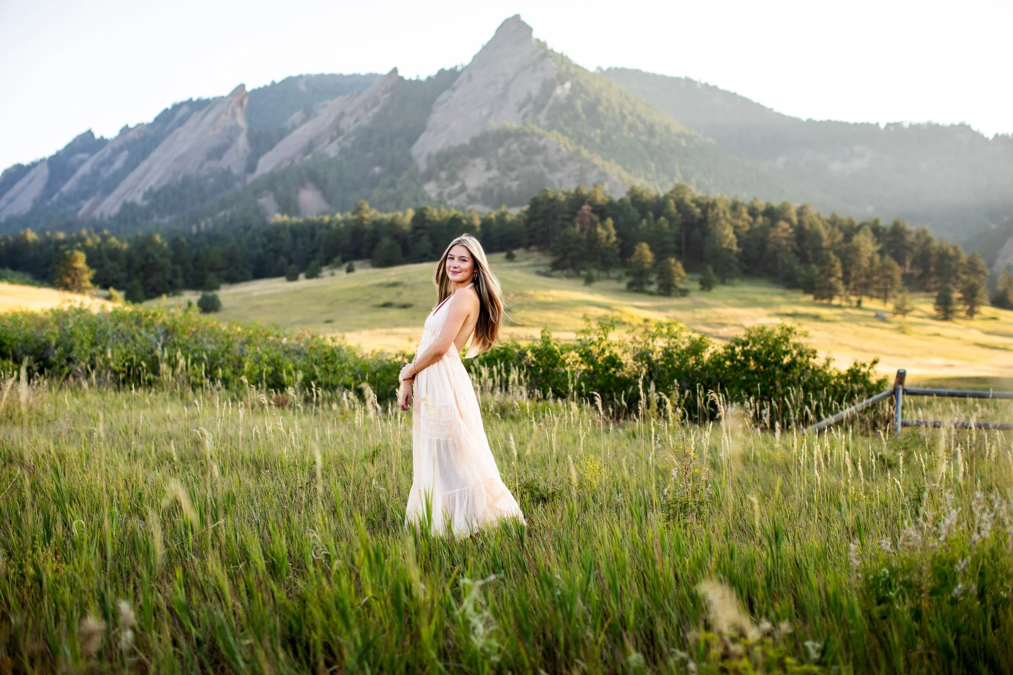 High school senior girl standing in a beautiful green field in front of the front range mountains at Chautauqua Park in Boulder Colorado