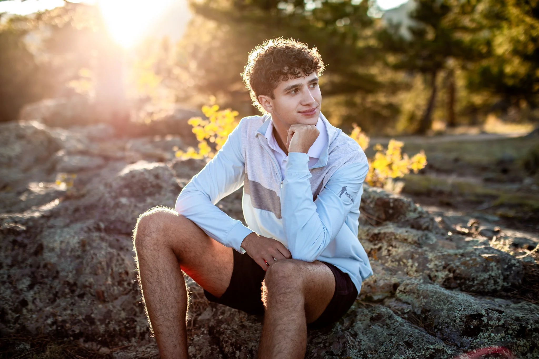 Boulder Senior Photographer captures image of high school senior boy sitting on rocks with the sunsetting behind him