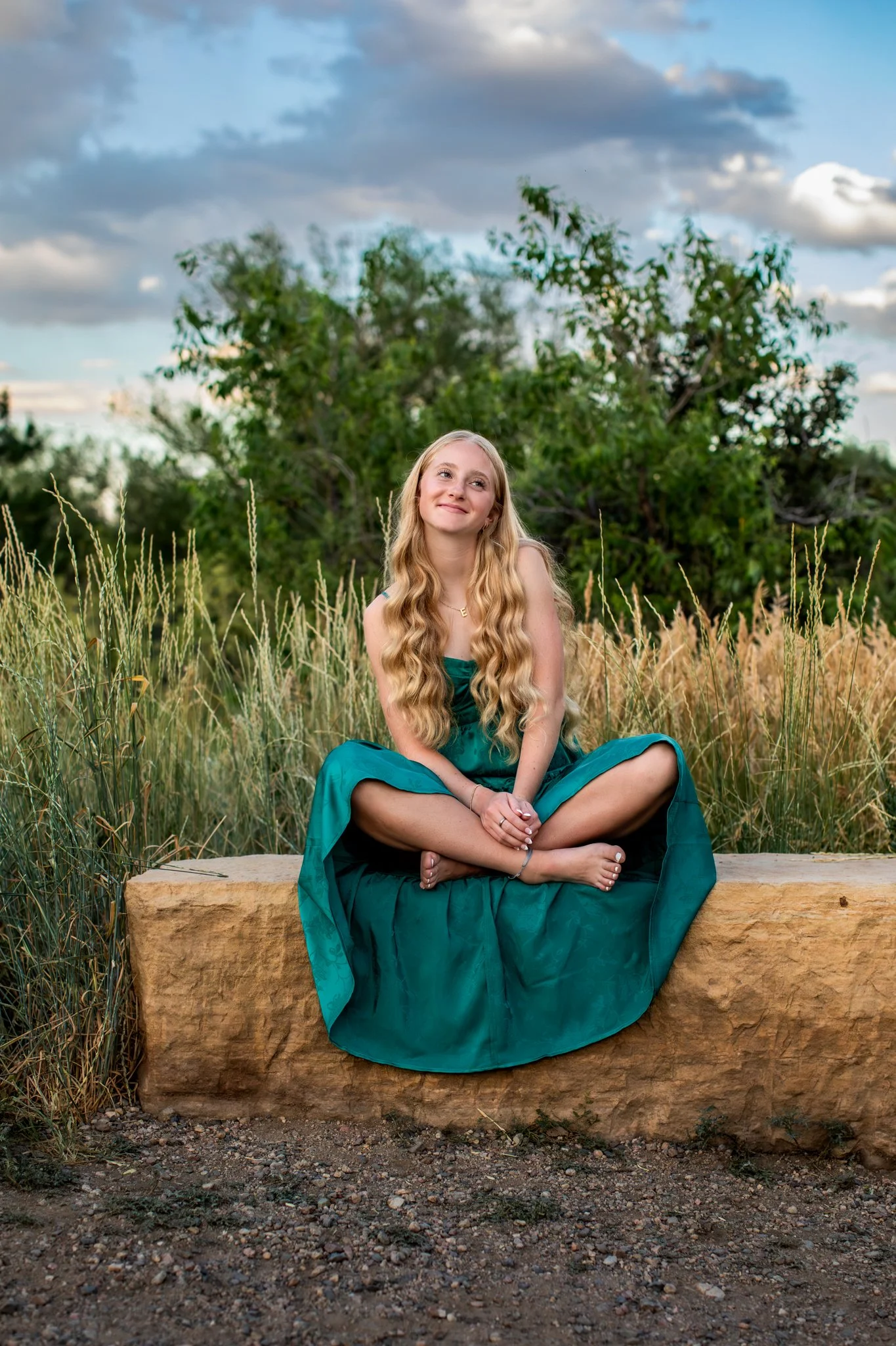 Senior Portrait Photographer takes picture of High School Senior girl sitting on a rock in a green maxi dress.